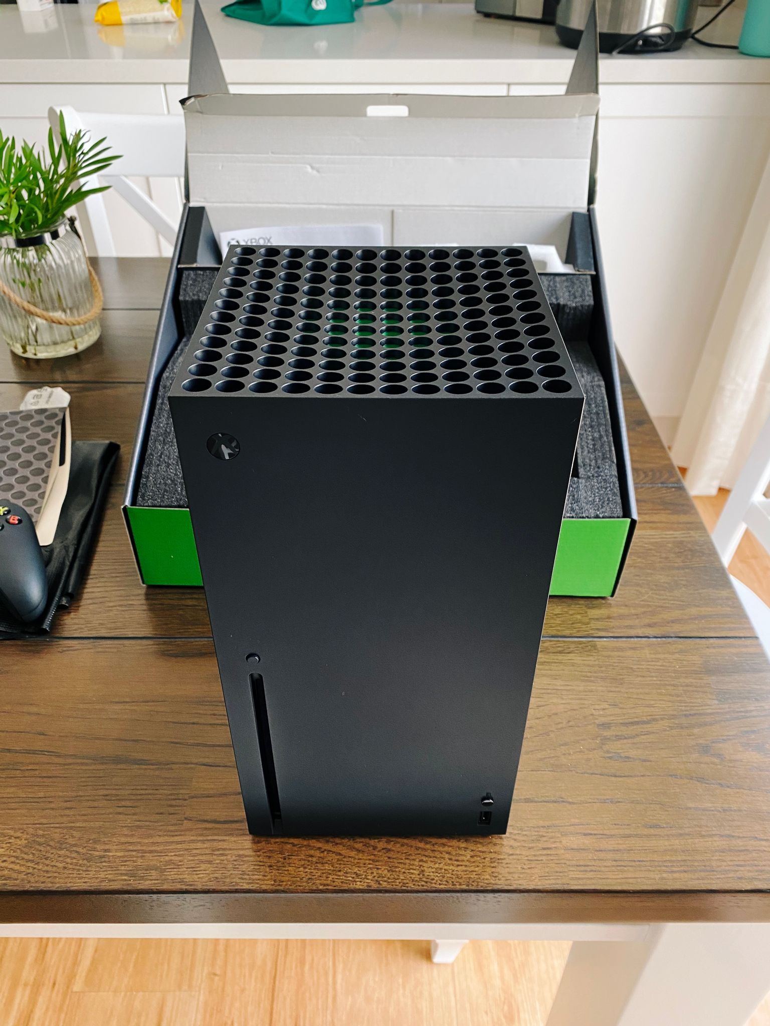 A photo of an Xbox Series X standing in front of the Xbox Series X box.