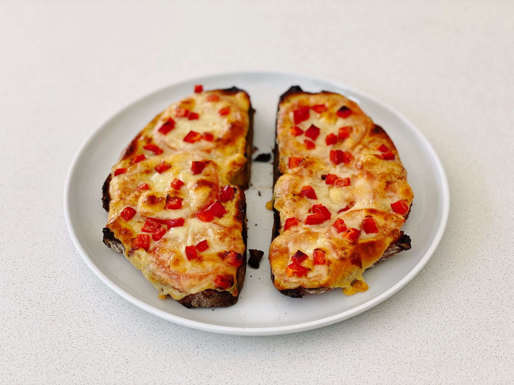 A photo of the two pieces of bread that comprise my cheese and tomato toastie with a bunch of small chopped pieces of capsicum sitting on top of the cheese.