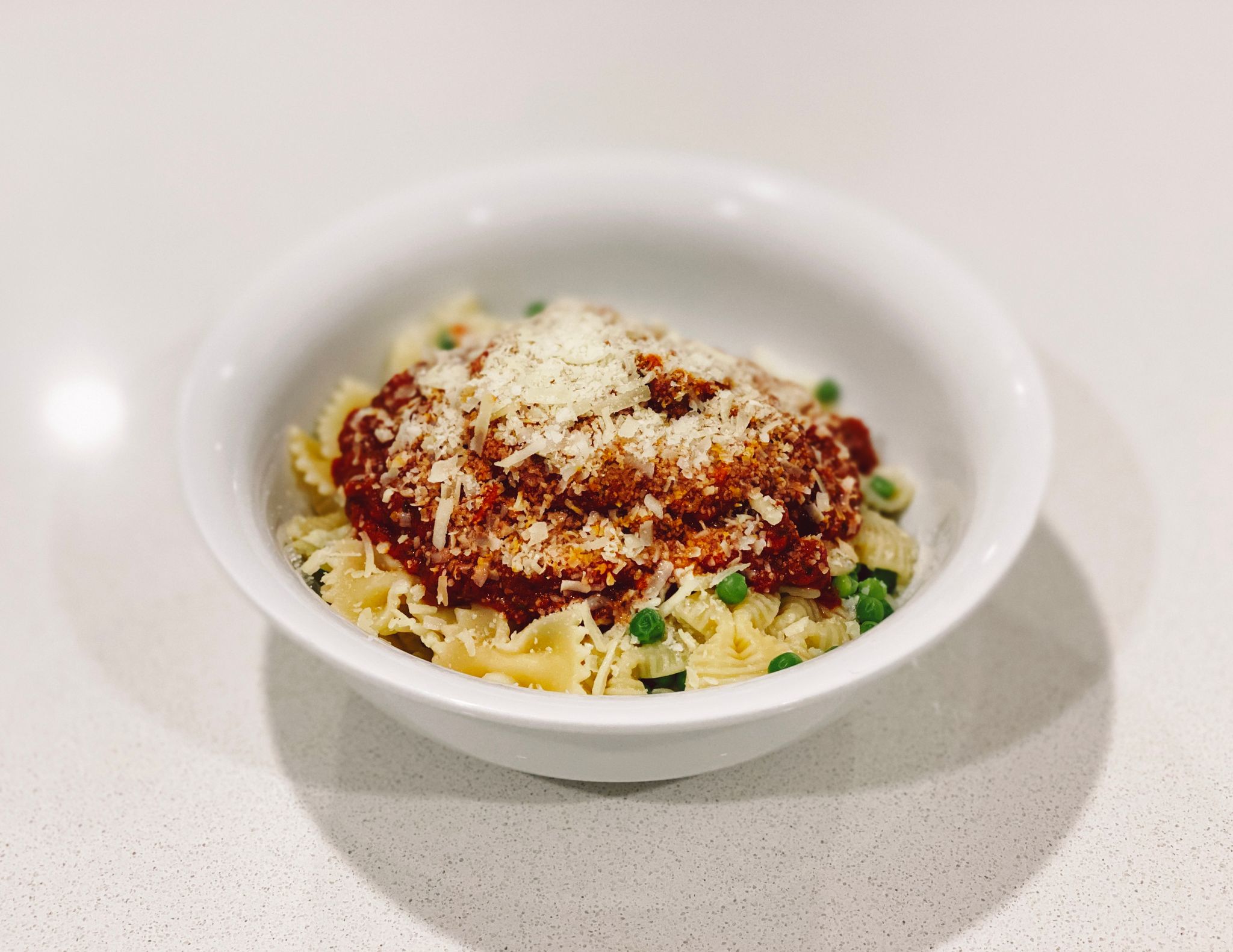 A photo of a bowl of bow-tie pasta with peas mixed in, with a big helping of tomato pasta sauce on top, and the whole thing topped by grated Parmesan cheese.