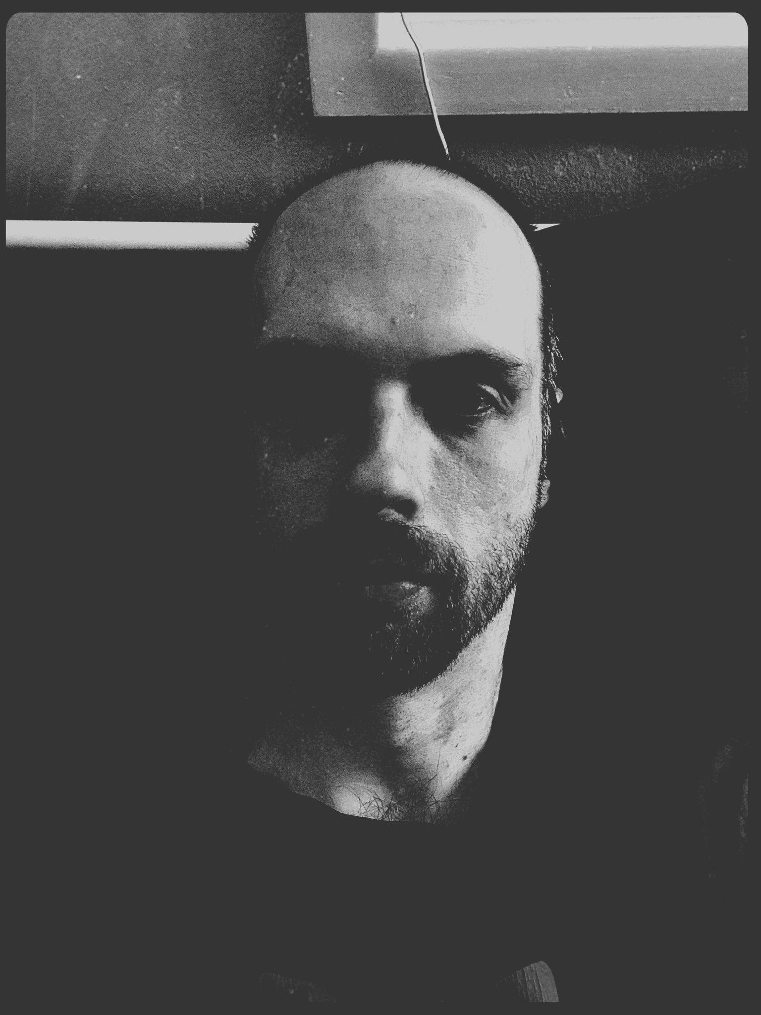 A selfie of me, a white man with a receeding hairline, a goatee, and the beginnings of a full beard. The photo is extremely dark and in in black-and-white.
