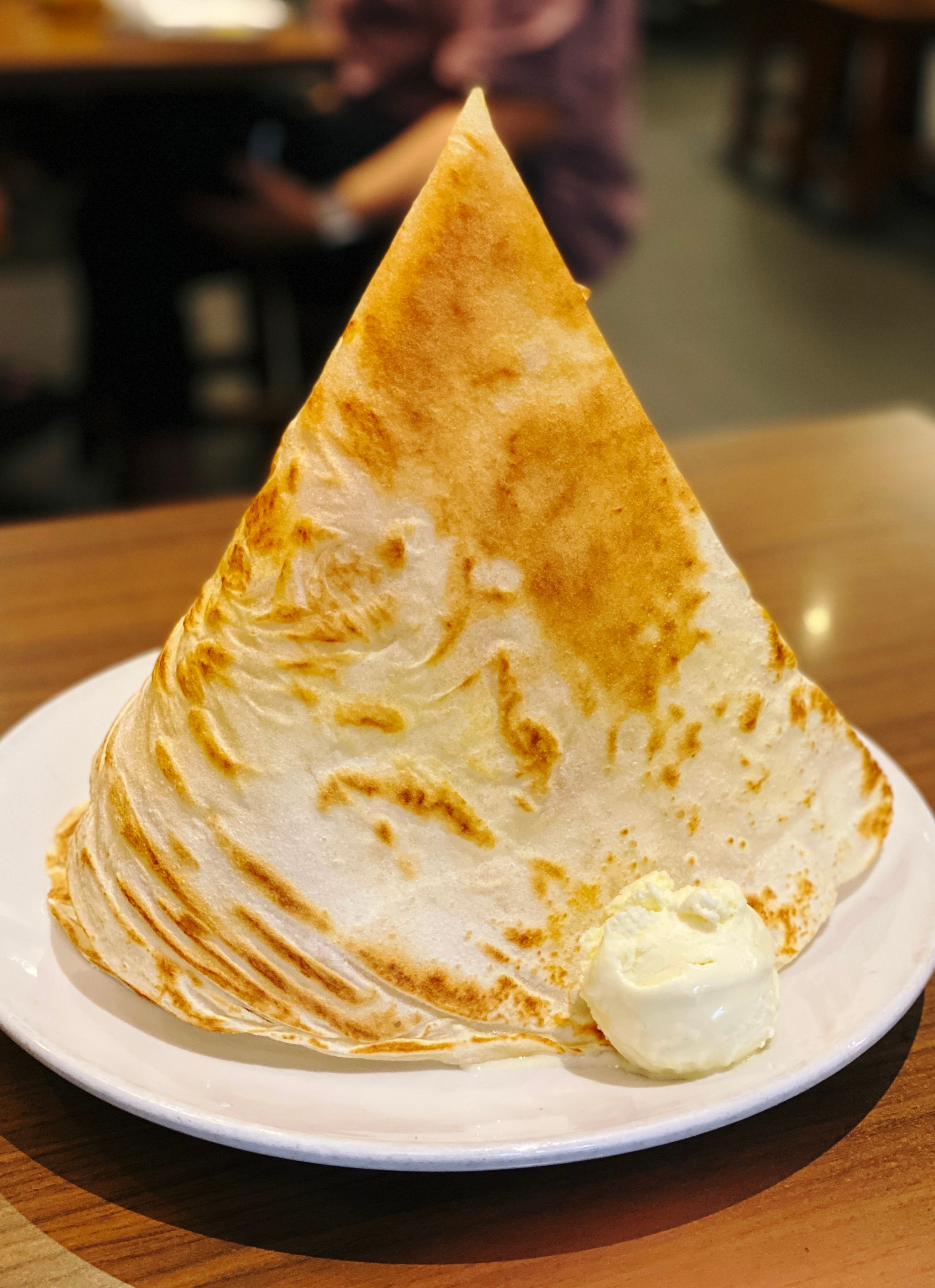 A photo of a roti tisu, which is a tall cone-shaped thin and crispy sugar-covered piece of deliciousness, sitting on a plate and dwarfing the scoop of ice cream that's sitting at the base of it.