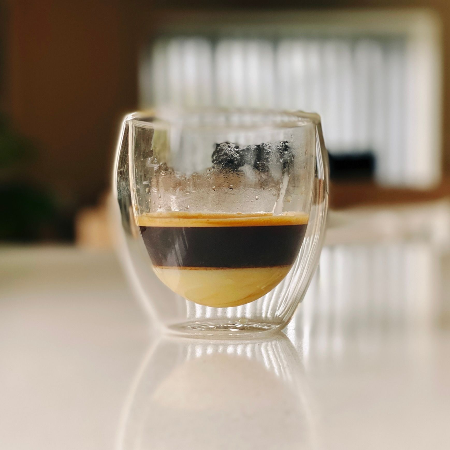 A photo of a fancy double-walled espresso glass with a layer of sweetened condensed milk sitting on the bottom and espresso sitting on top.