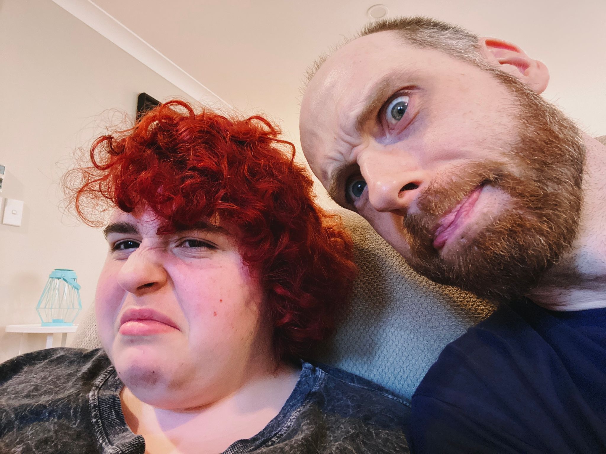 A selfie of me, a white man with a red beard and short hair, poking in from the side of frame, and Lily, a white girl with short and curly dyed-red hair and a look of mild disgust on her face.
