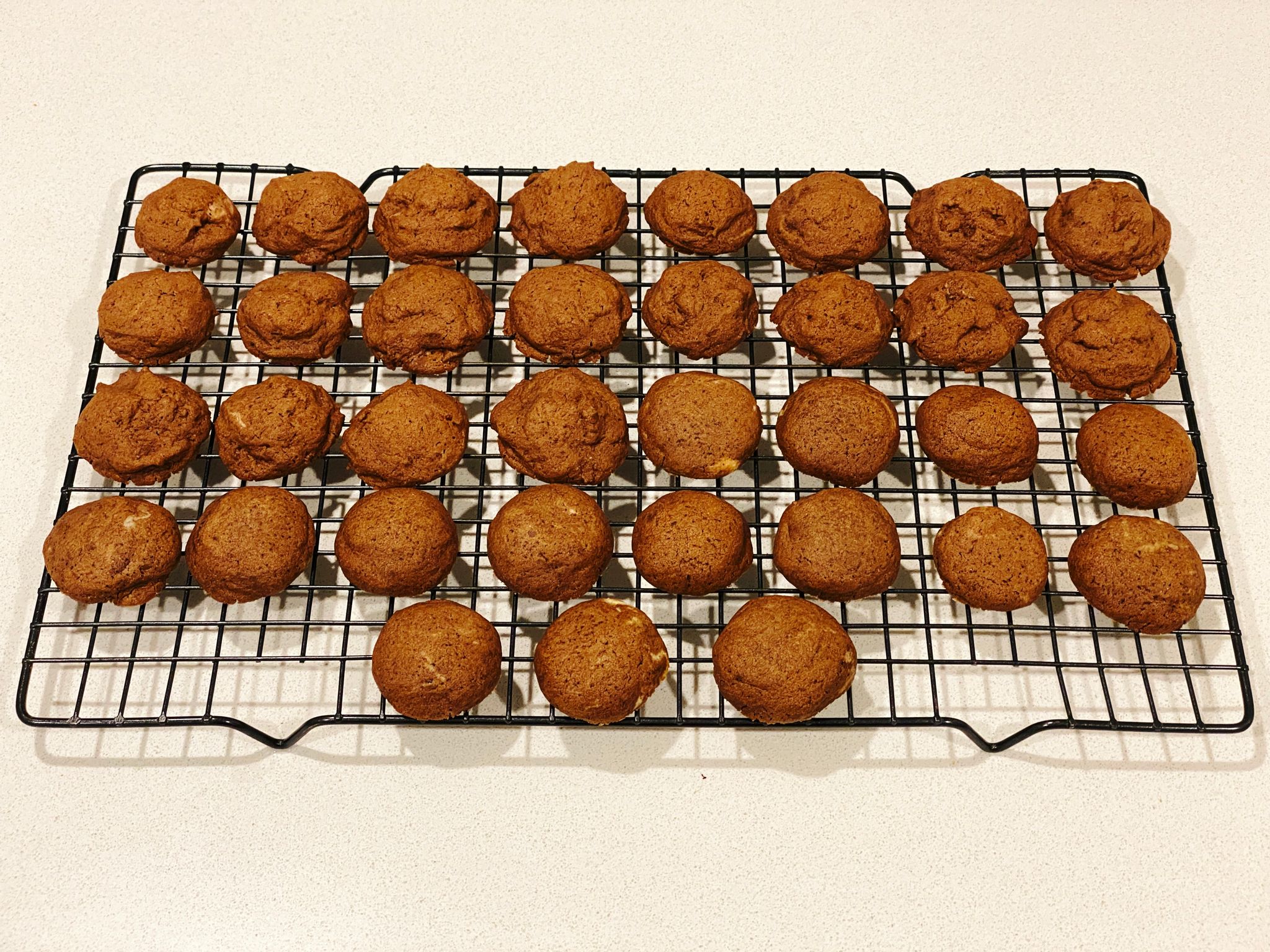 A photo of a bunch of small button-shaped chocolate cookies sitting on a cooling rack. The ones are the back are a bit munted, they're lumpy and more spread out than the ones in the front.