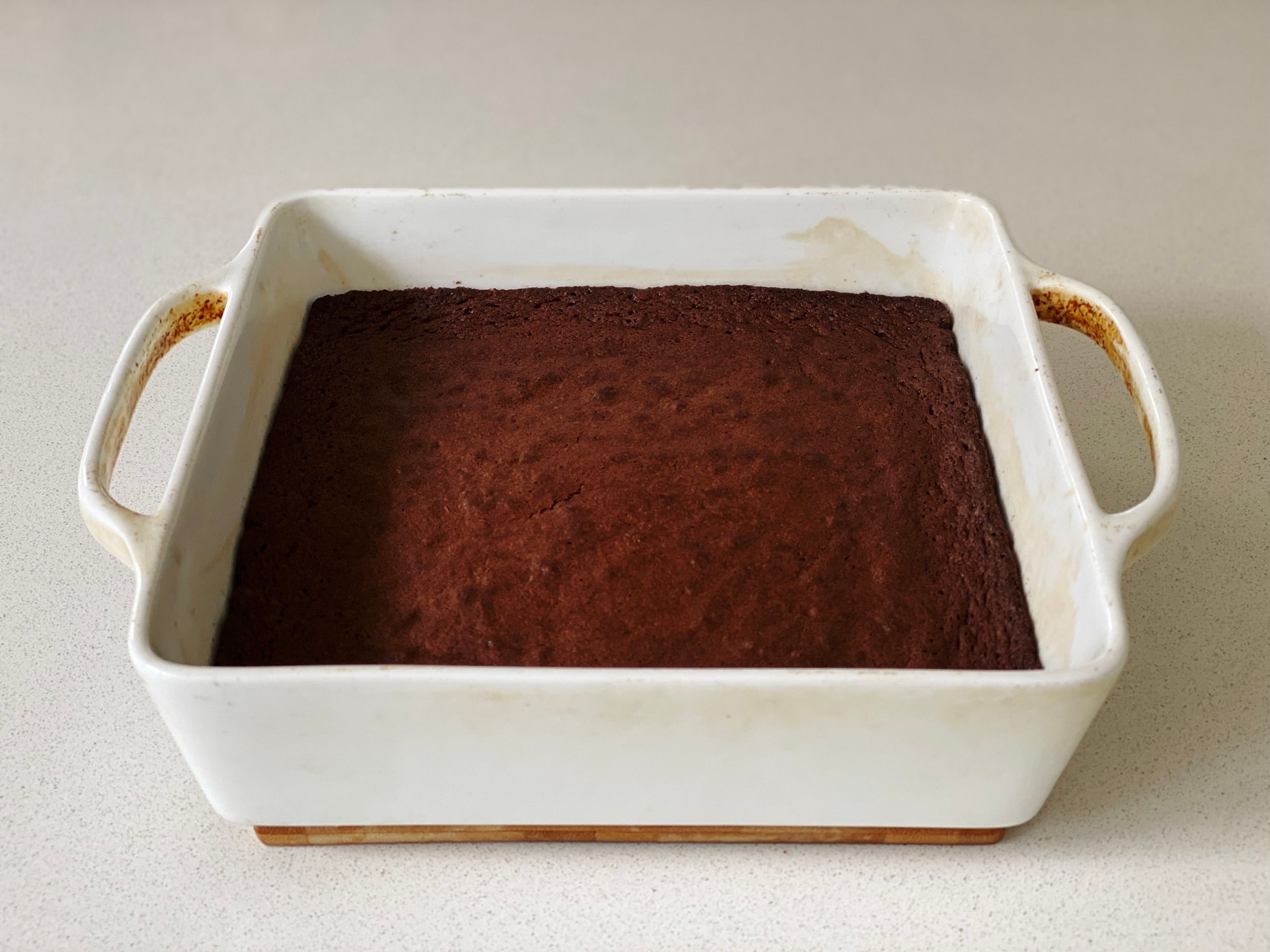 A photo of a square white ceramic baking dish with delicious-looking chocolate brownie in it.