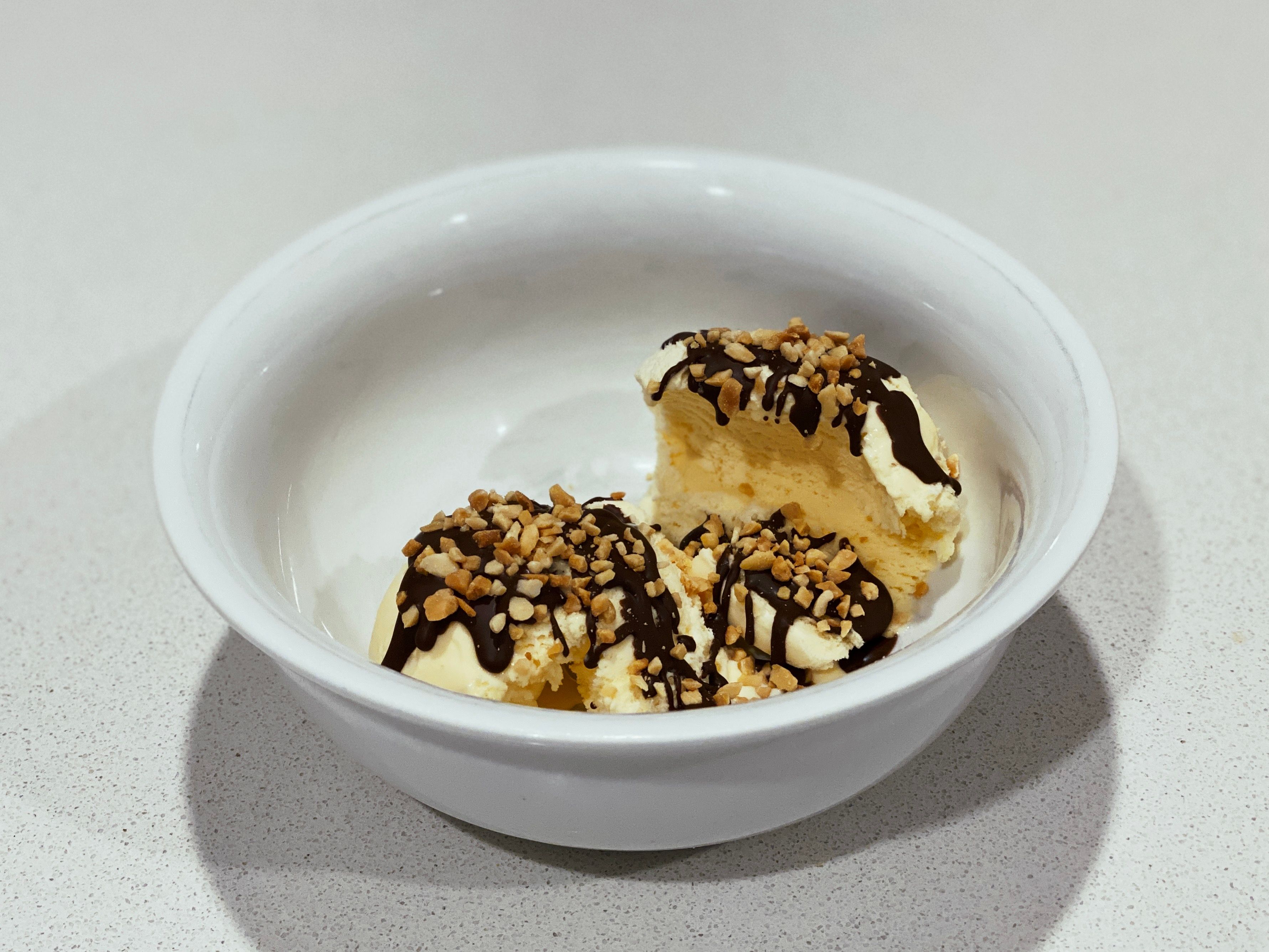 A photo of a bowl of vanilla ice cream topped with Ice Magic and crushed peanuts.