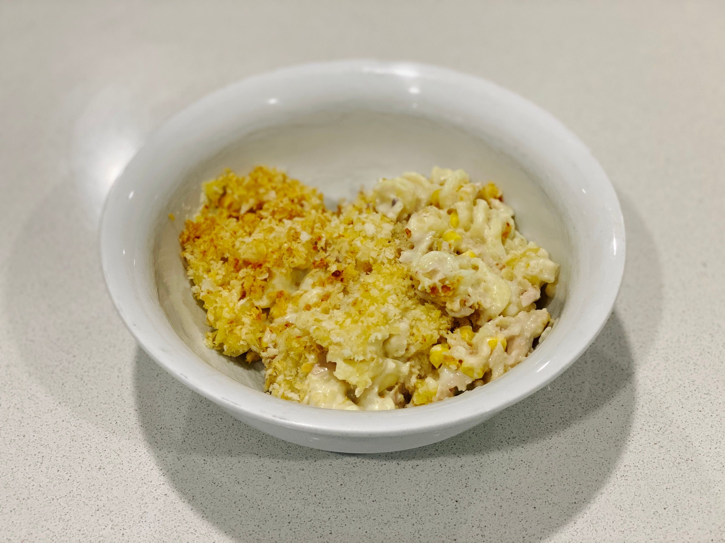 A photo of the tuna mornay in a bowl. Here you can see that underneath the topping it consists of spiral pasta with chunks of tuna and pieces of corn in a thick white sauce.
