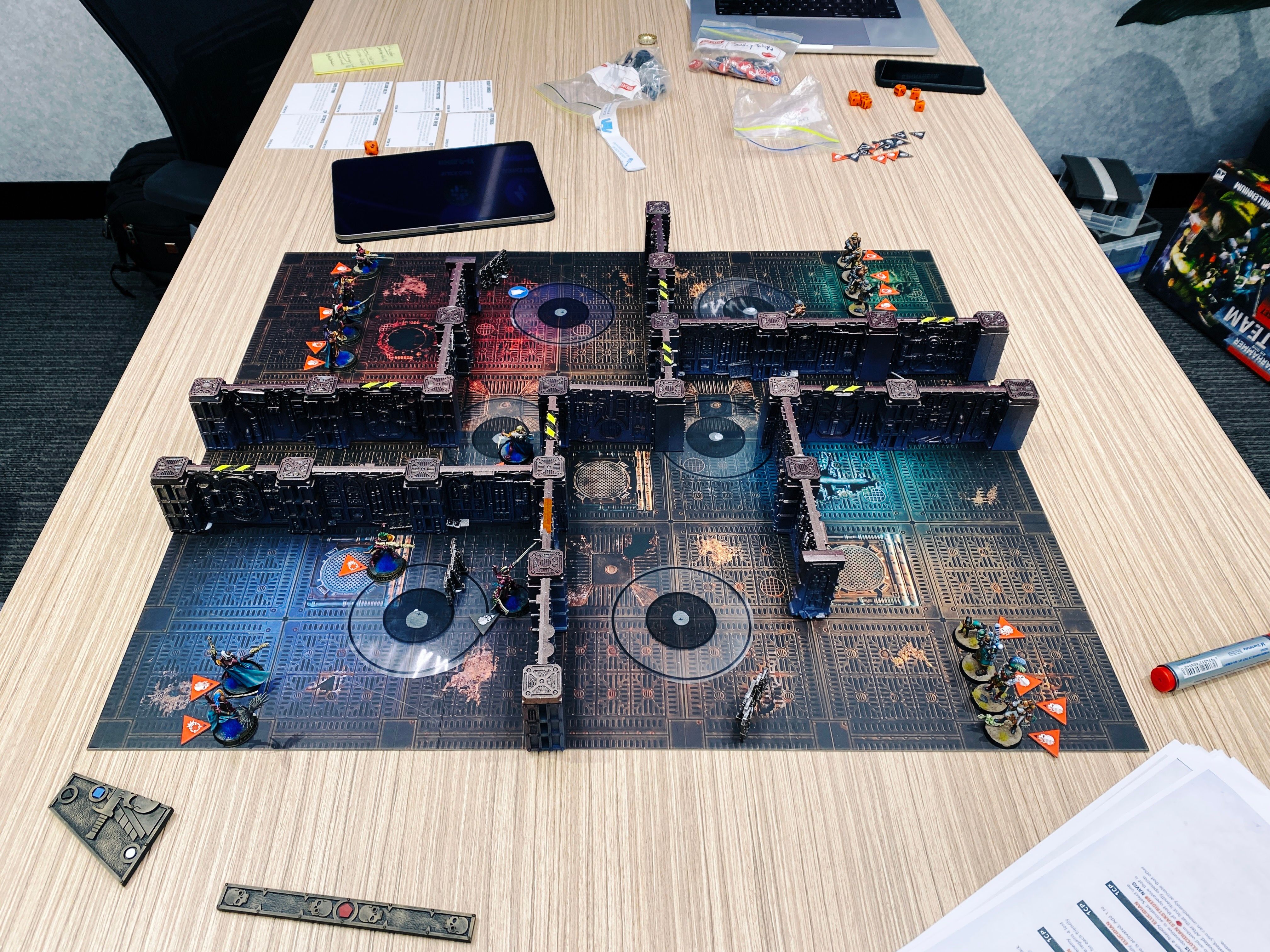 A photo of a game of Warhammer 40,000: Kill Team. The board looks like the metal of the inside of an ancient steampunk starship, and the terrain is a bunch of walls all connected together in the same steampunk style to form number of interconnecting rooms. On the left are my forces, the Aeldari (think space elves) in elegant fuchsia-coloured armour, and facing them on the other side of the board are the Elucidian Starstriders, a motley assortment of lightly armoured humans.