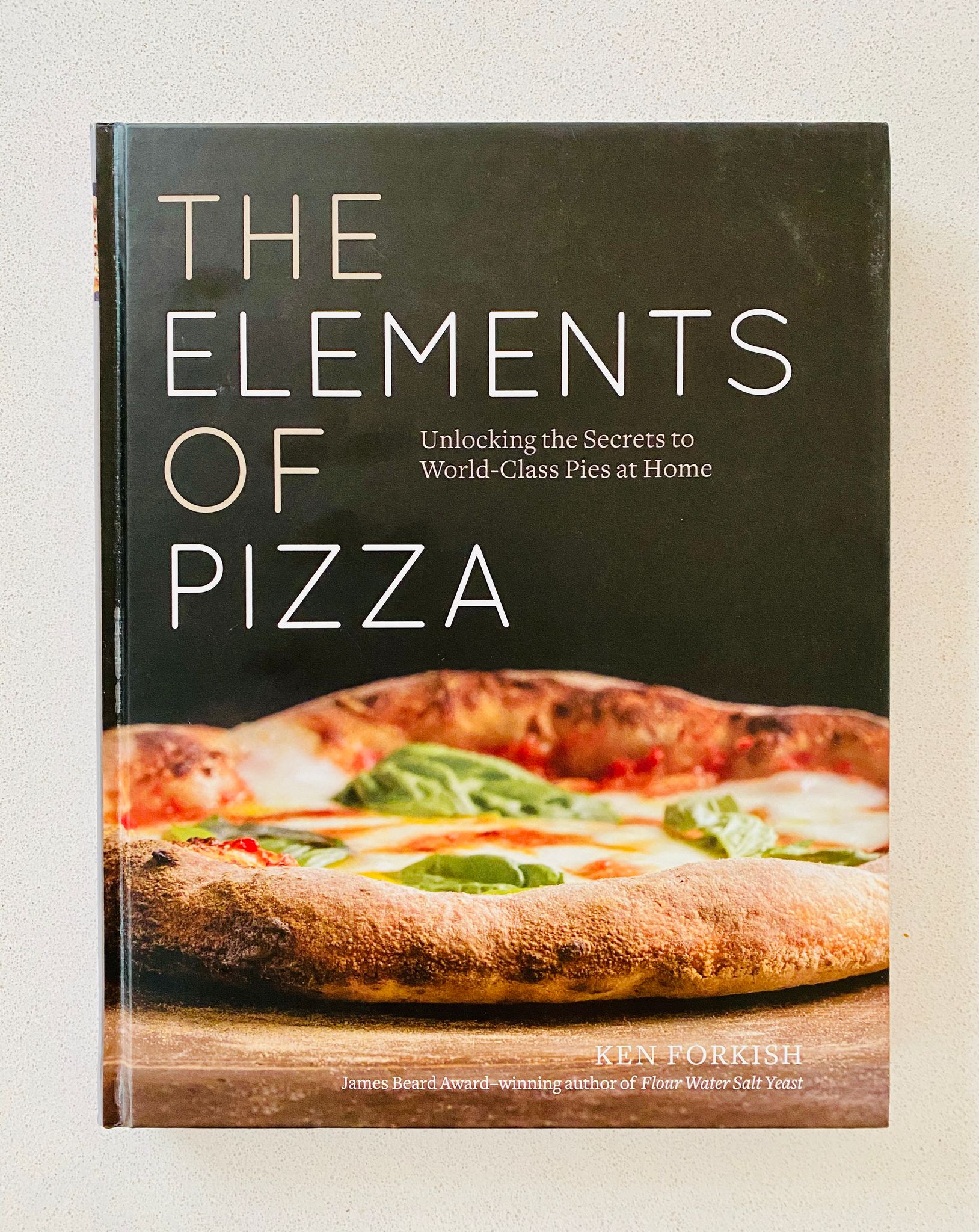 A photo of the cover of a book called "The Elements of Pizza". It has a very arty-looking photo of a delicious-looking pizza on it.