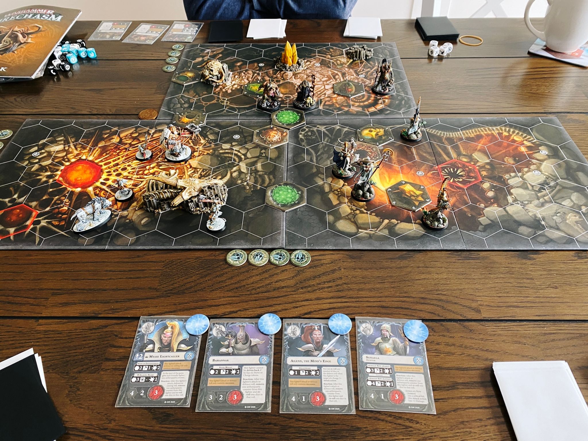 A photo of a three-player game of Warhammer Underworlds, a hex-based board game with miniatures and cards.