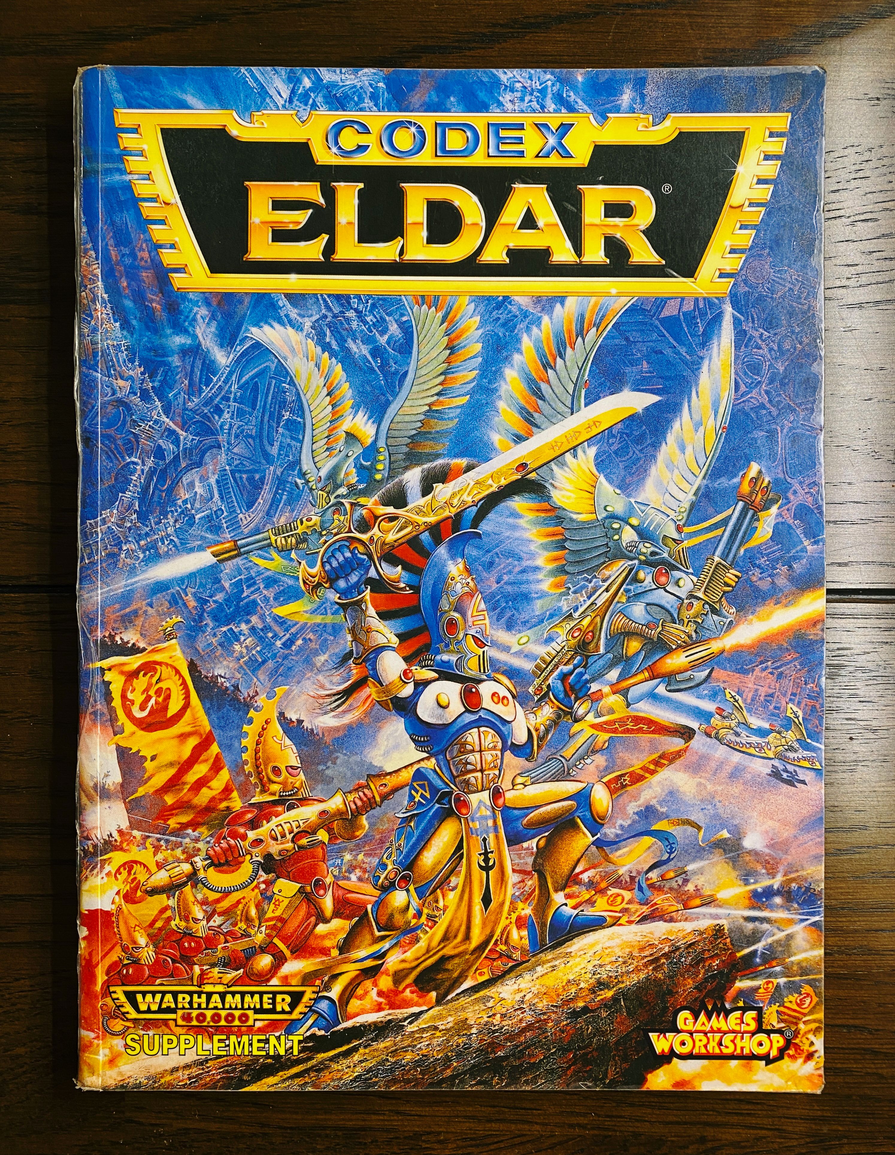 The cover of the Warhammer 40,000 Second Edition army rulebook for the Eldar. The artwork on the front is classic Games Workshop, an exquisitely-armoured Eldar warrior standing atop a piece of rock, wielding a sword above his head. There's TONS of warriors in the background and all sorts of tanks and guns being shot, though they're all similarly elegant-looking Eldar warriors and tanks.
