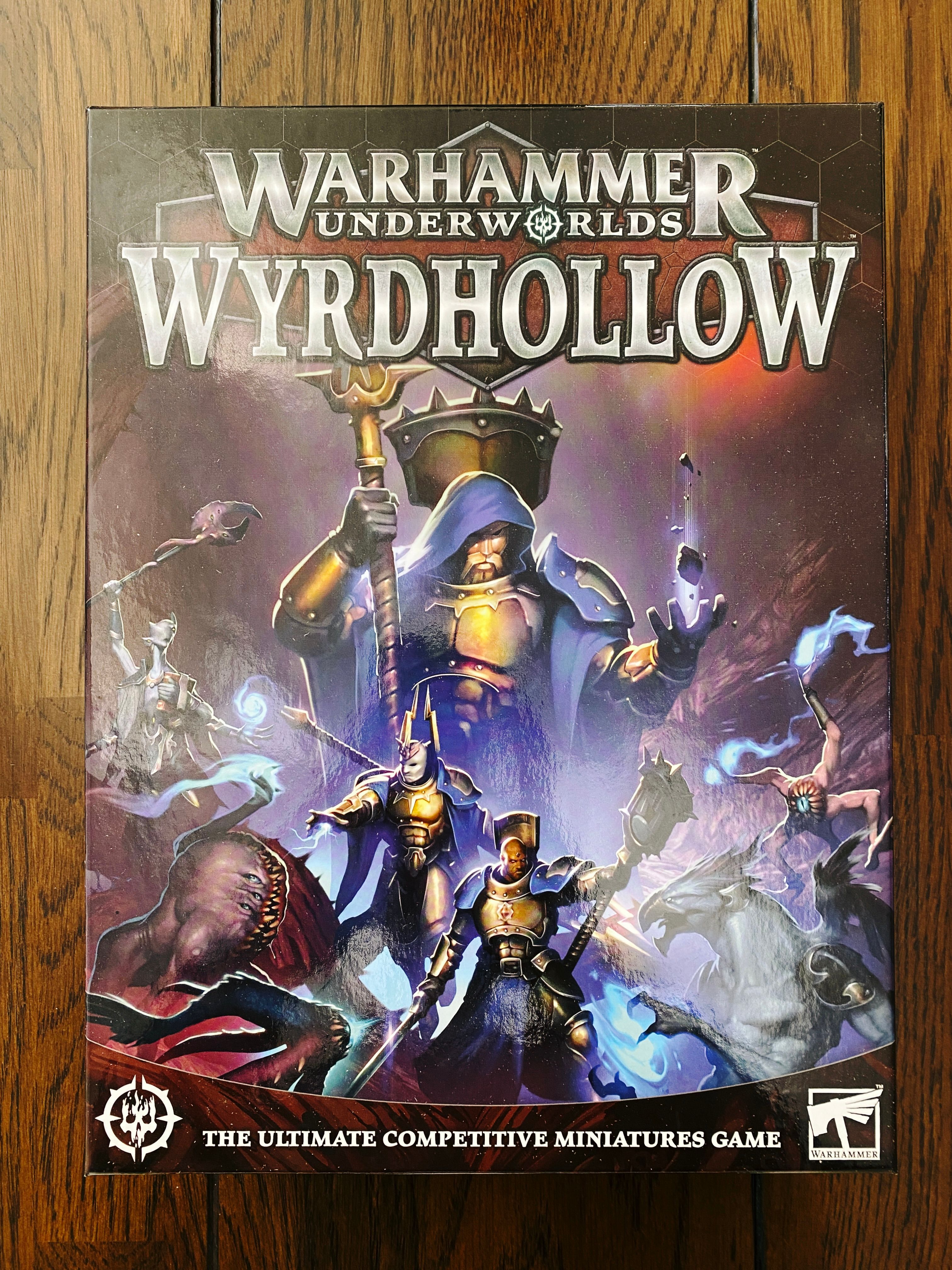 A photo of the front of the box of the new Warhammer Underworlds release. The artwork has a guy in golden armour with a big blue cloak with a hood standing there with a staff and casting some sort of magic, and below that are two more similar figures fighting off freaky-looking misshapen daemons.