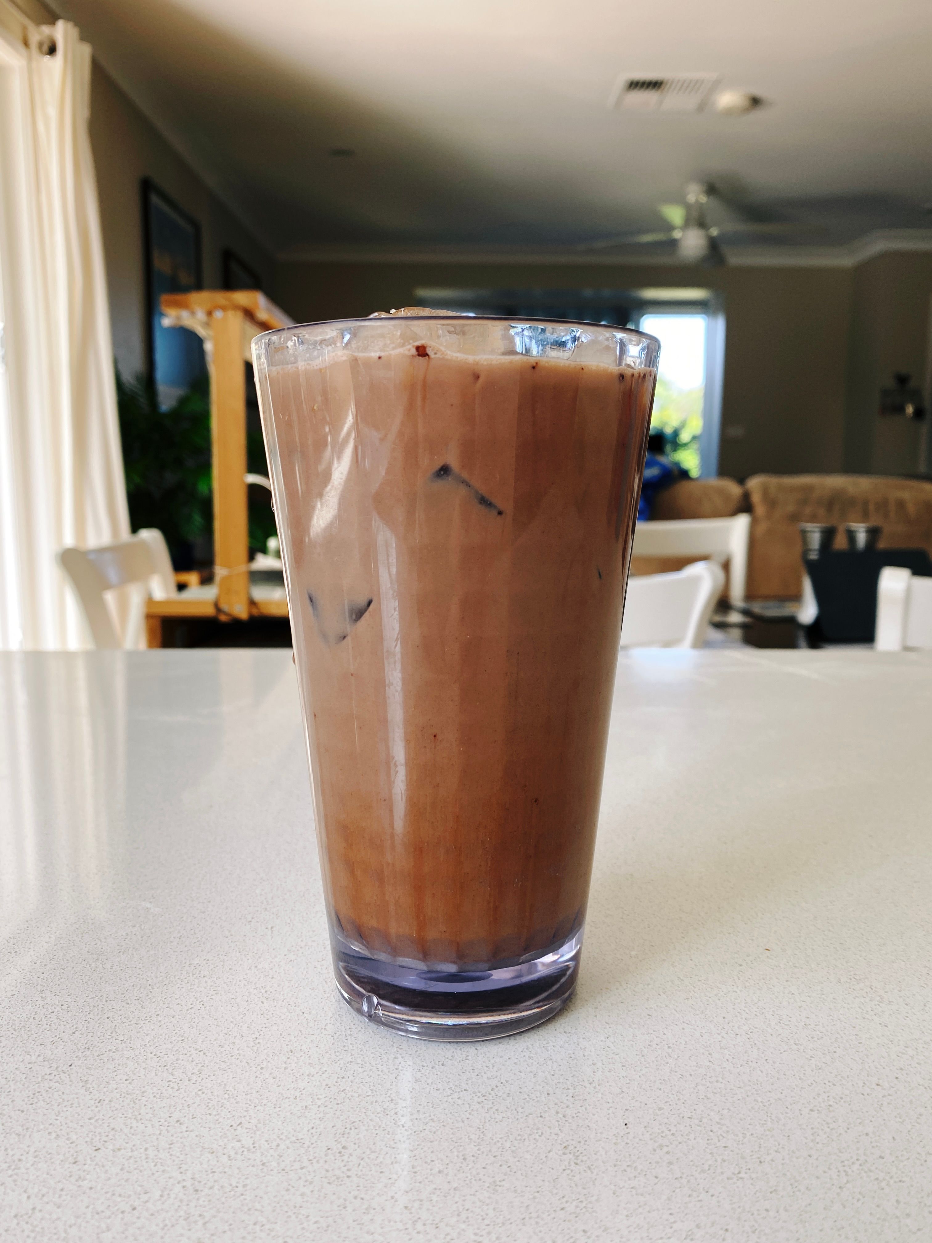 A photo of a tall plastic cup of iced mocha sitting on a benchtop.