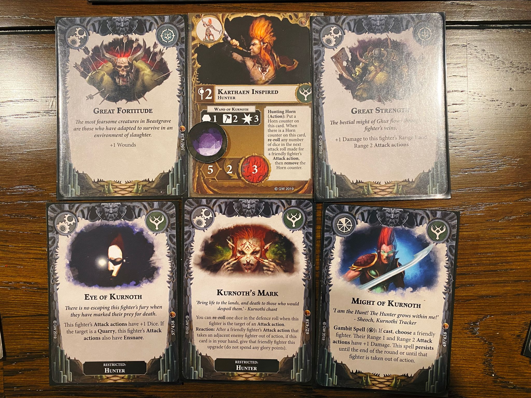 A photo of Karthaen's character card with a bunch of upgrades: Great Fortitude (+1 wounds), Great Strength (+1 damage), Eye of Kurnoth (+1 dice to attack actions), Might of Kurnoth (a temporary +1 damage upgrade), and Kurnoth's Mark (grants the ability to re-roll one dice in the defence roll).