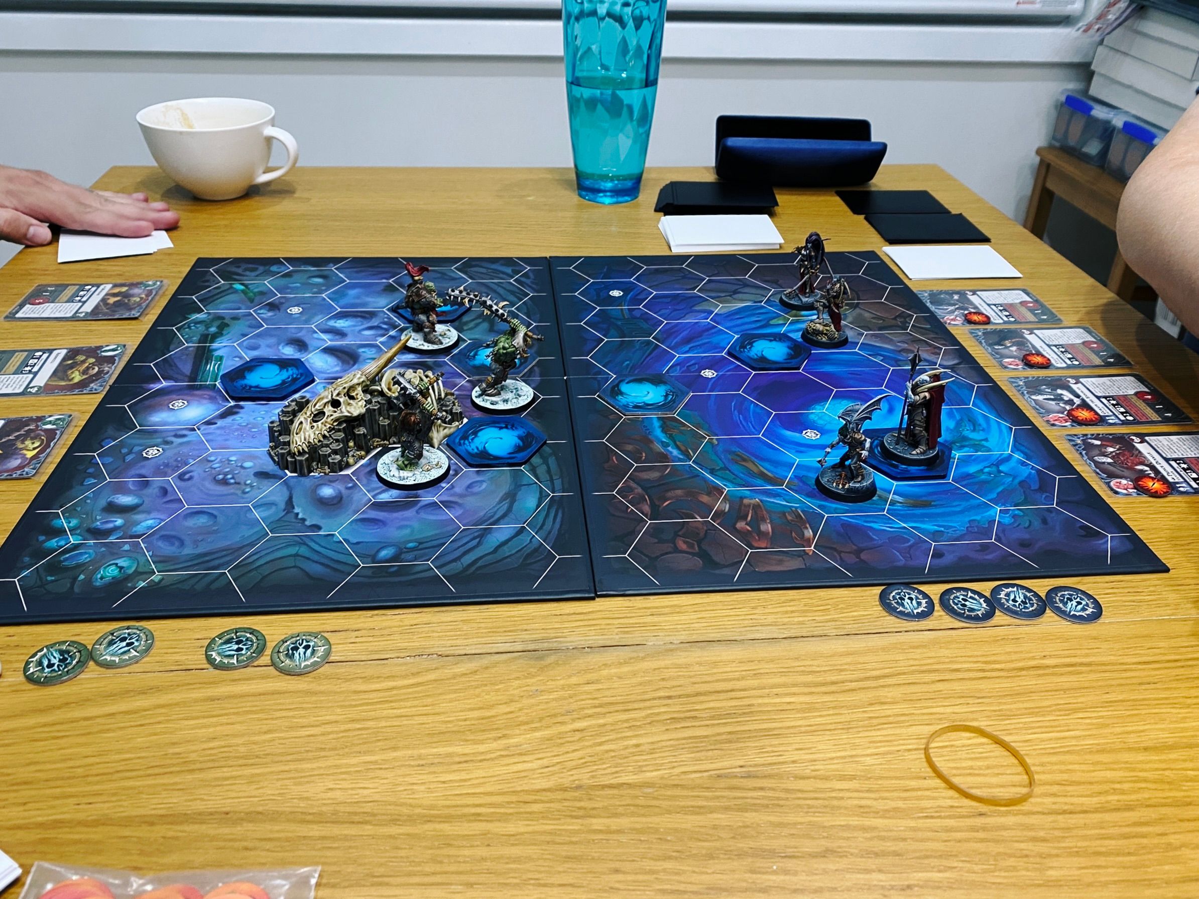 A photo taken side-on of a Warhammer Underworlds game board with three armoured orks on the left very aggressively positioned towards the middle of the board, and four elegant vampires on the right.