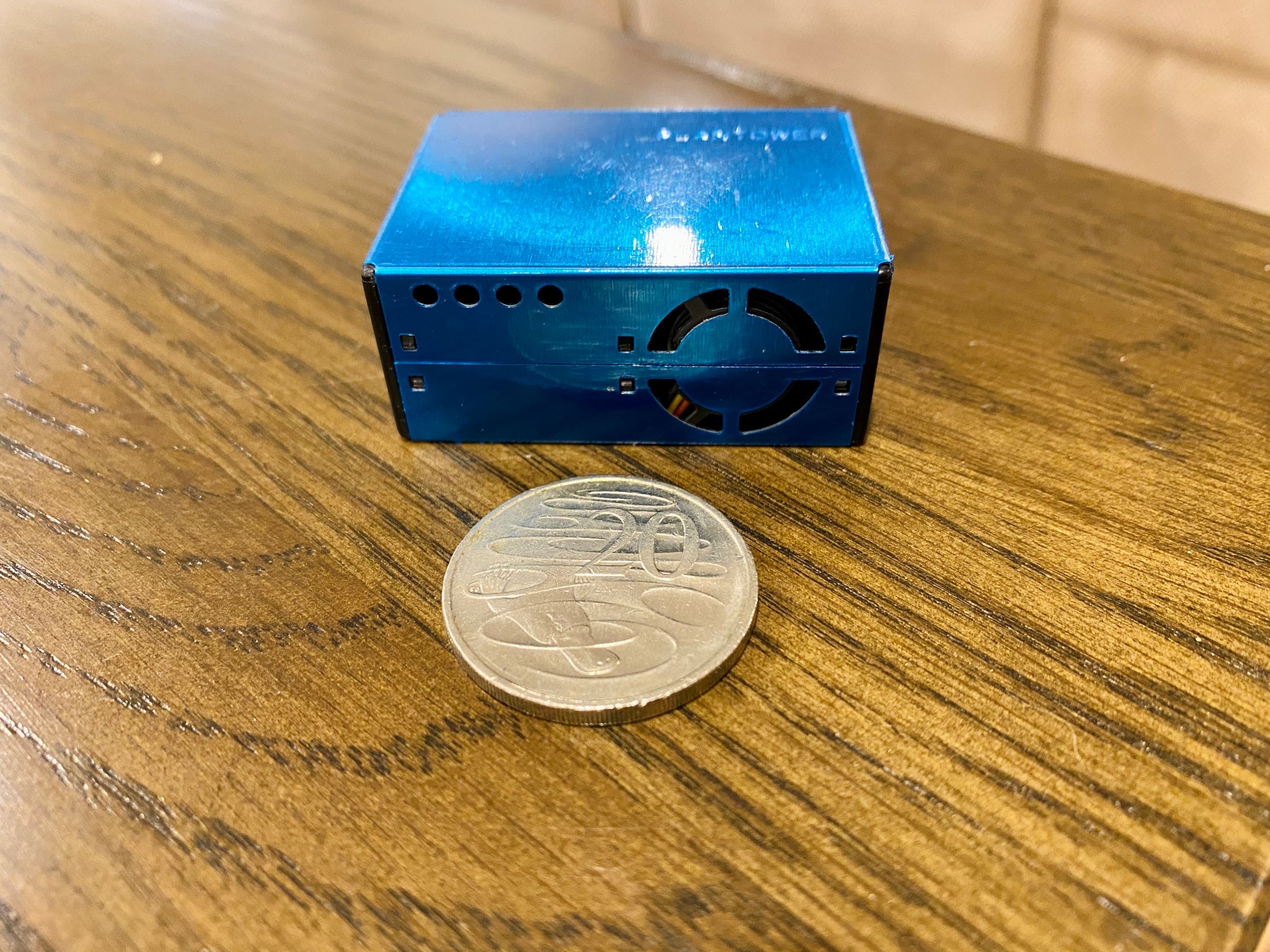 A photo of a blue box with a fan vent in it. An Australian 20c coin is sitting in front of it, and the coin is about a third of the size of the box.