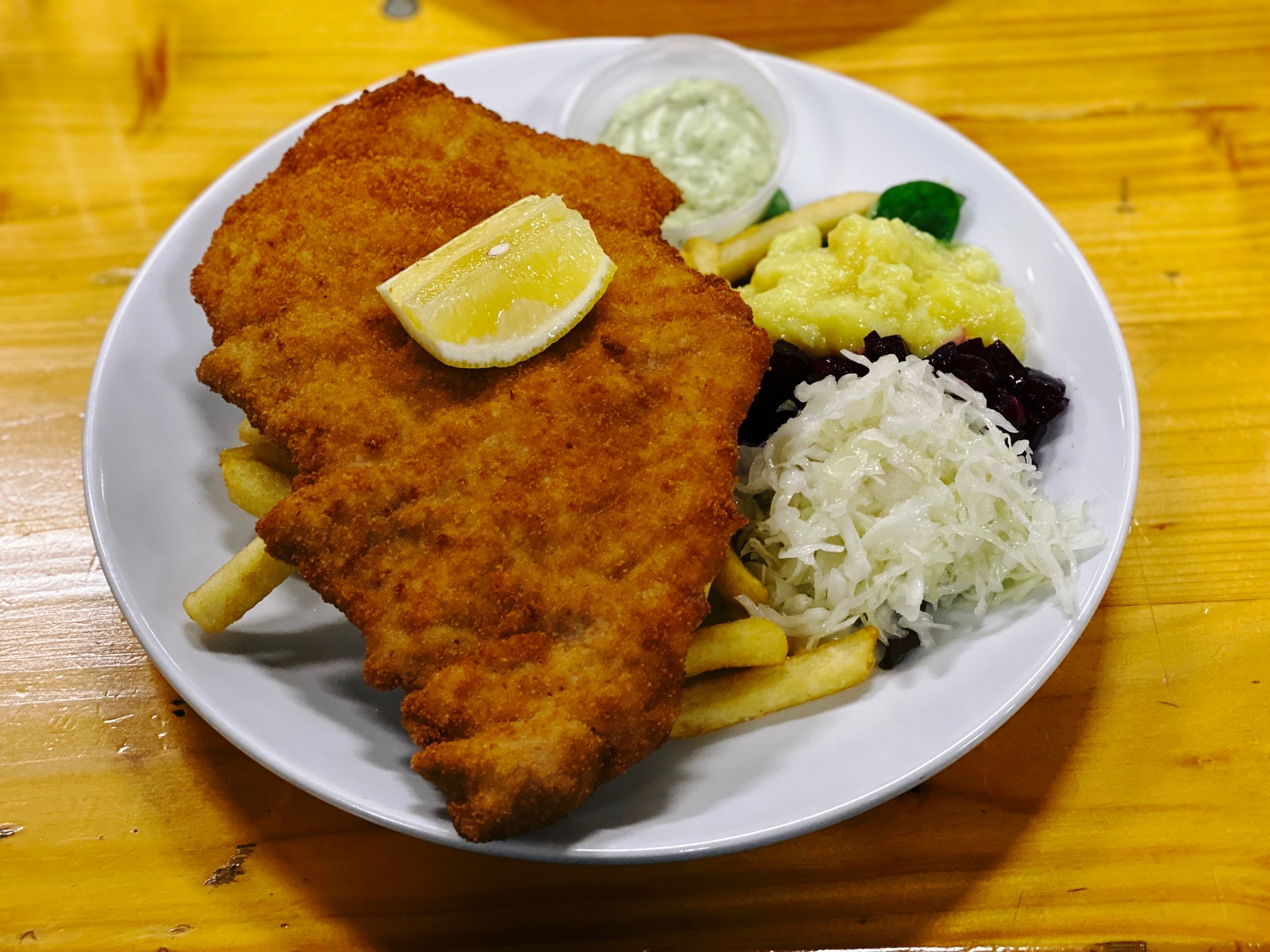 A photo of a pork schnitzel on top of chips, with some sort of pickled cabbage (it didn't taste like sauerkraut) and pickled beetroot things with a pasta salad thing as well.