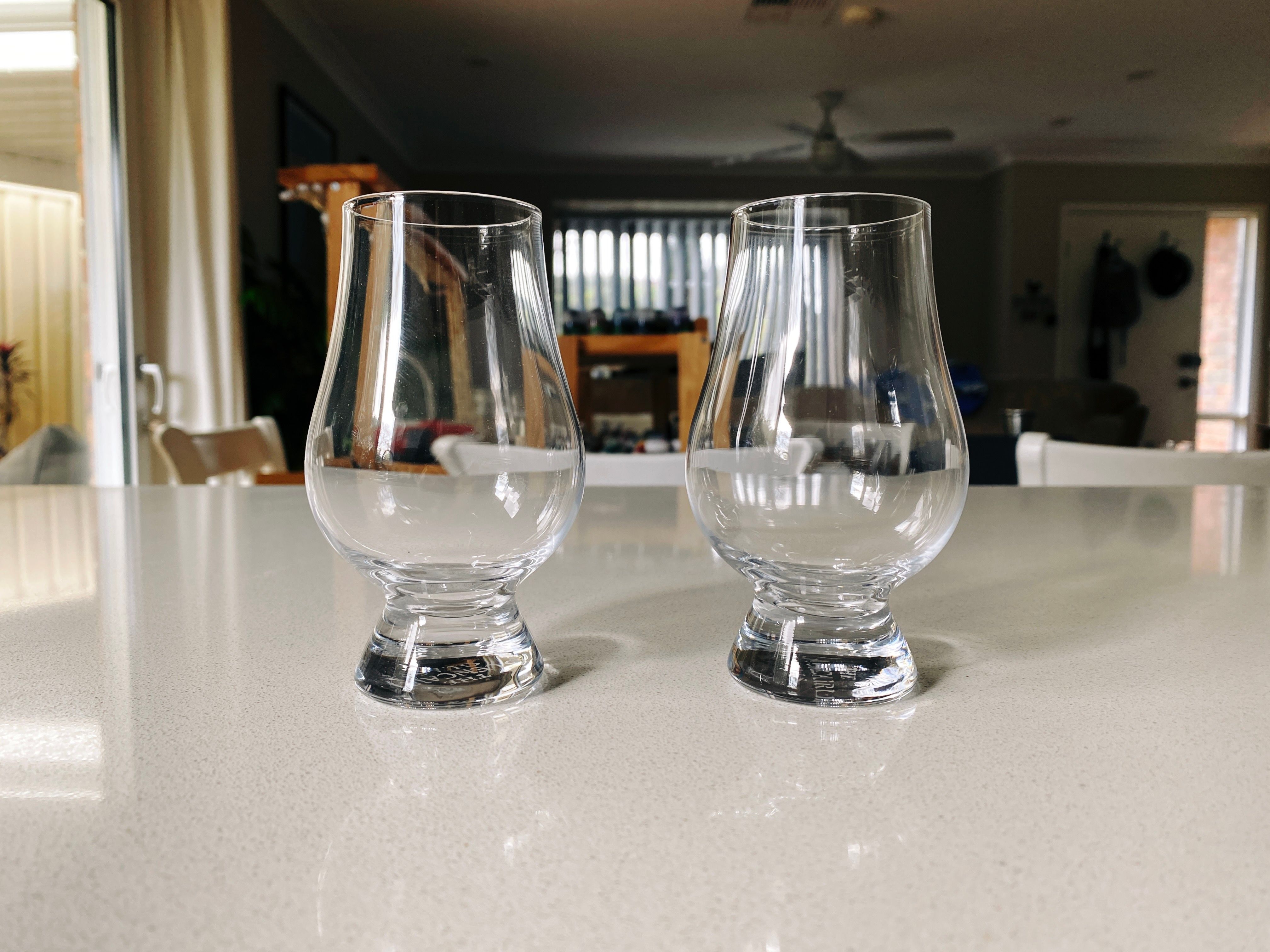 A photo of two glasses sitting on a kitchen countertop. They're pear-shaped, with a middle and base that's wider than the top.