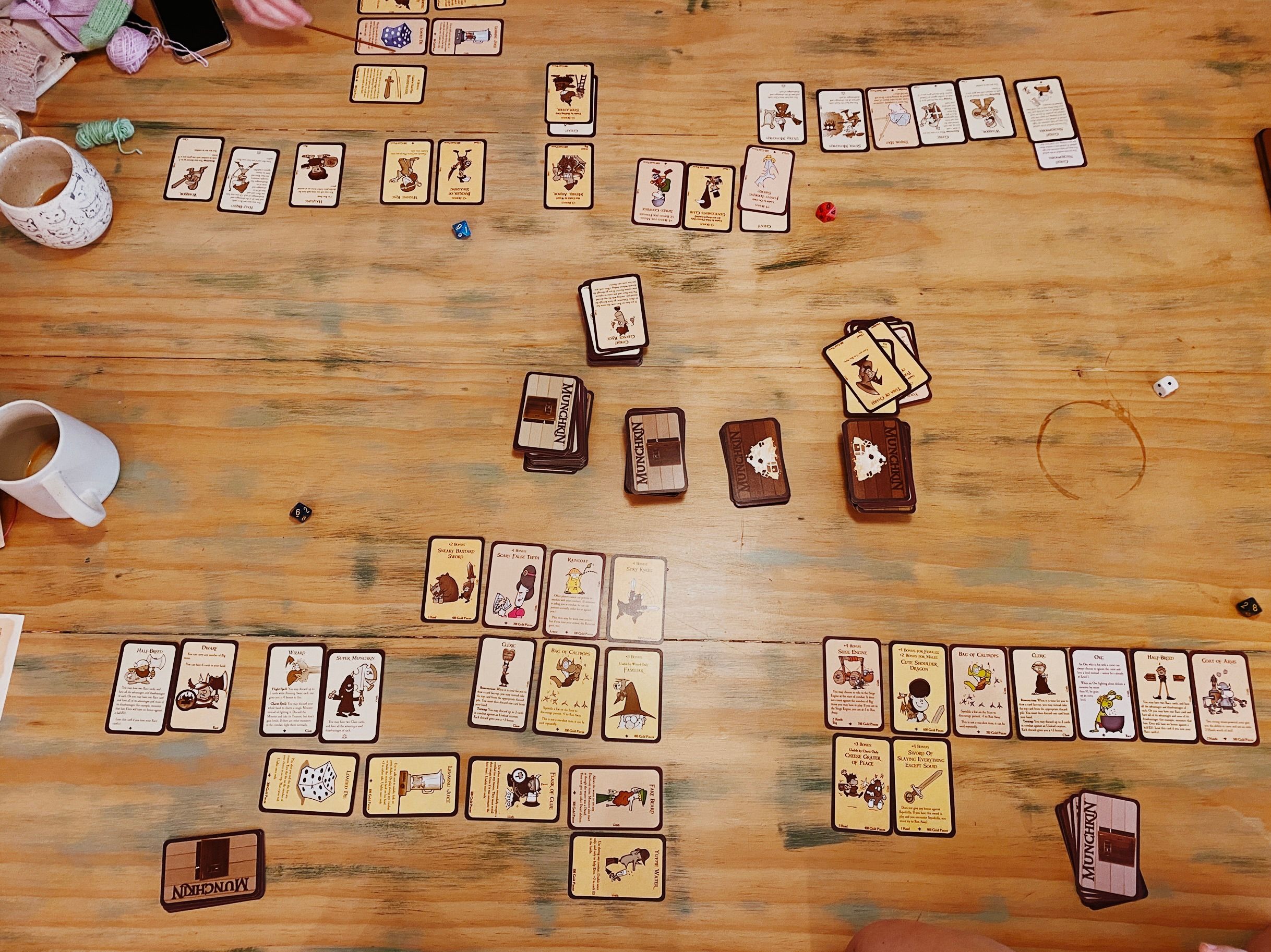 A photo taken from above a table of a four player game of the card game Munchkin. It's been in progress for a while everyone has lots of cards.