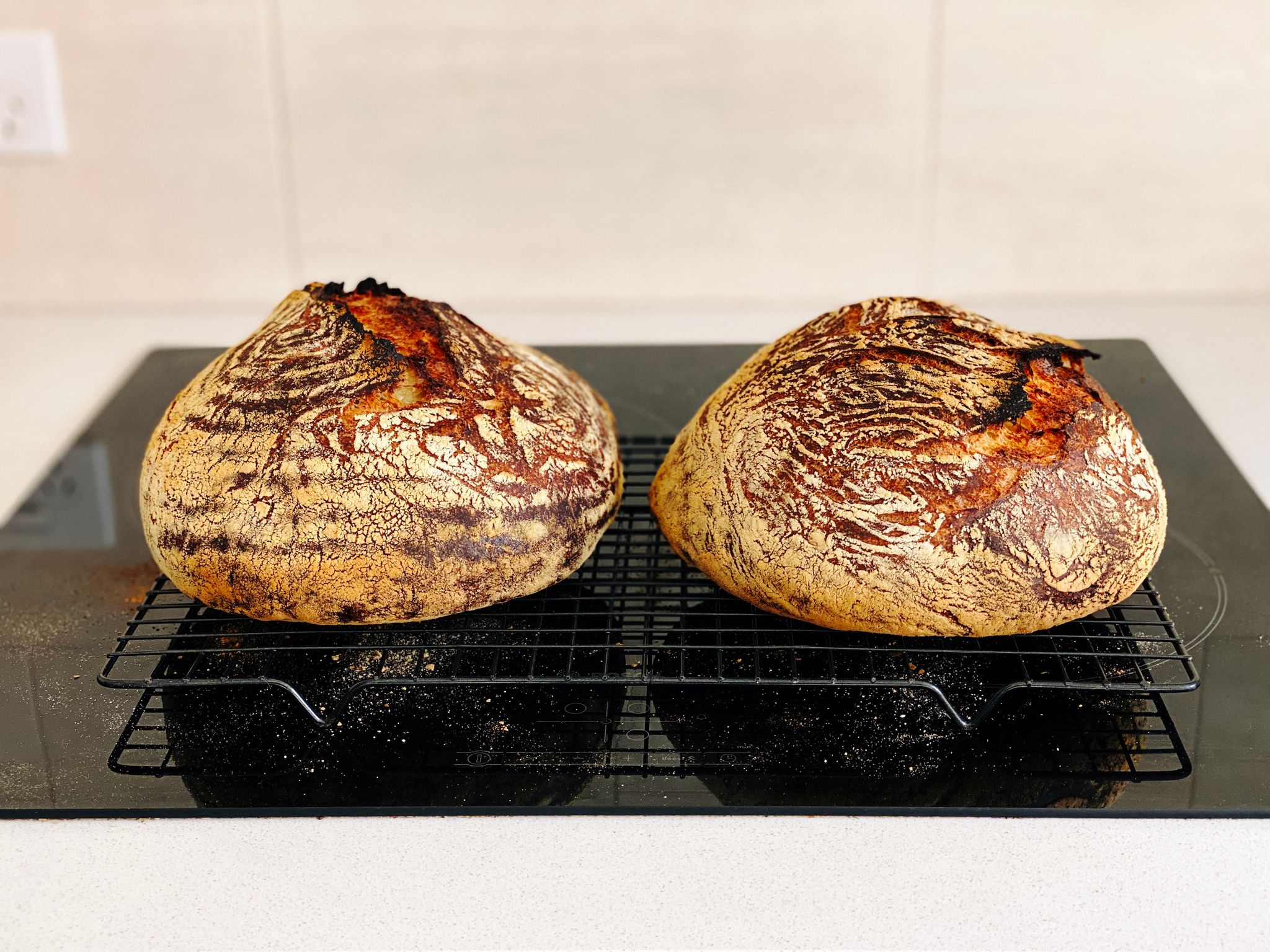 A photo of two round dark brown loaves of bread sitting on a cooling rack.