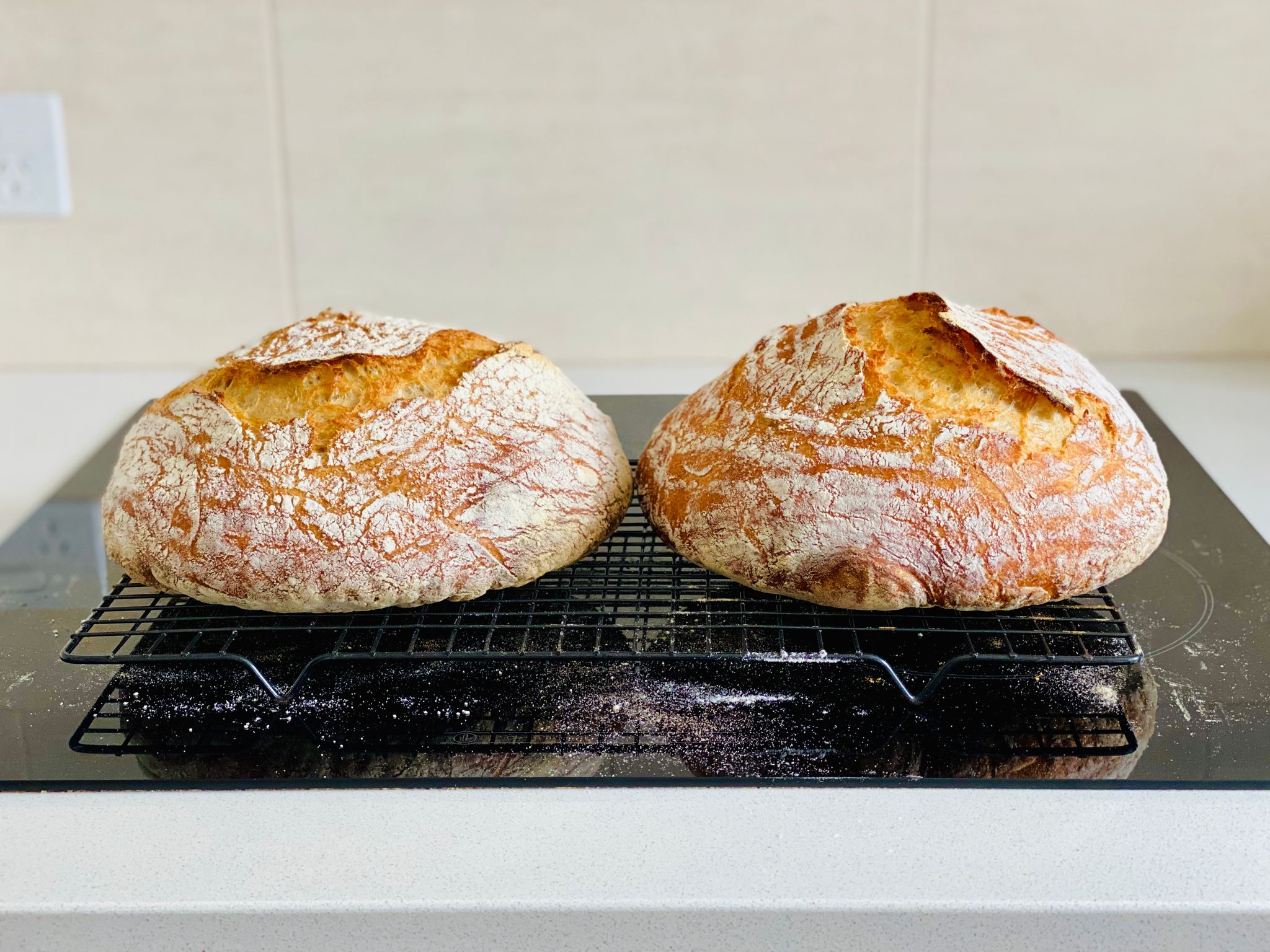 A photo of two round golden brown loaves of bread dusted with flour sitting on a cooling rack.