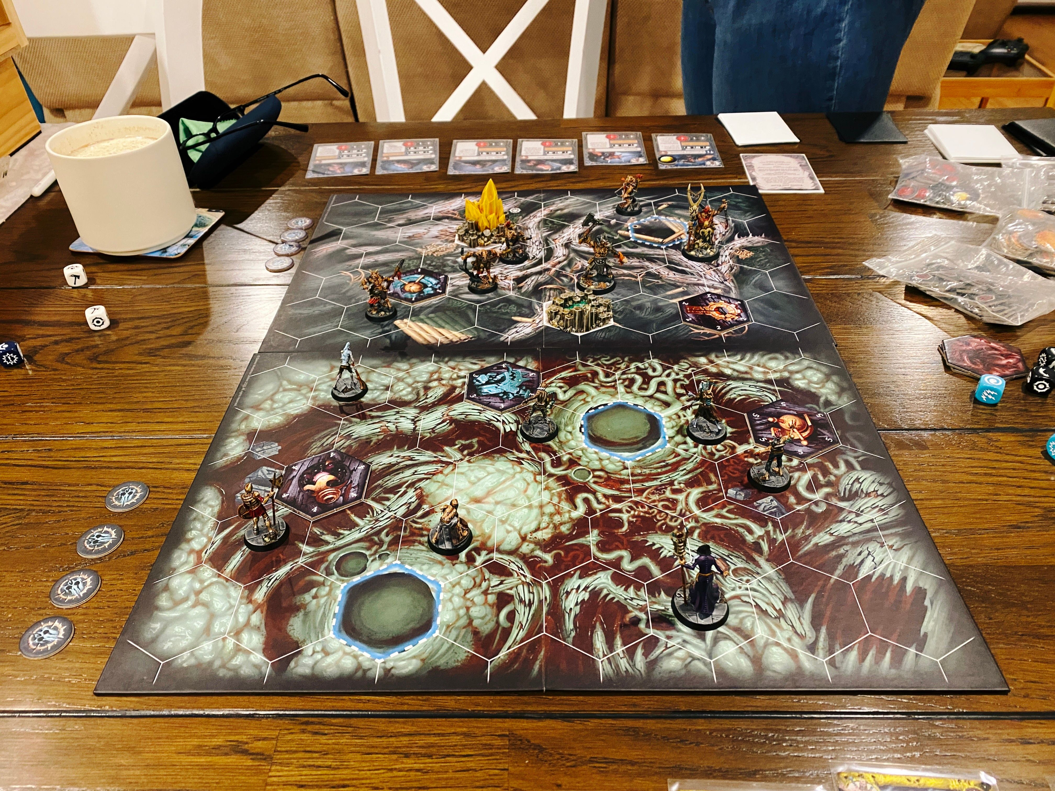 A photo of a Warhammer Underworlds game board. The artwork looks like a bunch of huge tree roots and on one side they look like they're going down into a river of blood. On the side closest to the camera are six zombies and a zombie master in a flowing purple cloak, and on the other side are six beastly goatmen.