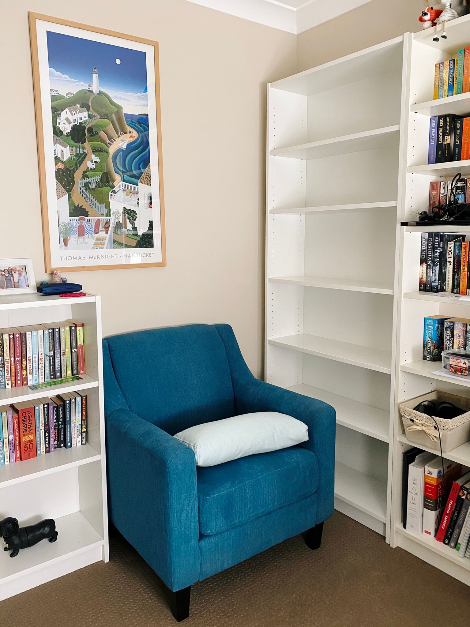 A photo of an empty white IKEA Billy bookshelf sitting next to a full-size one, with a blue armchair next to it.