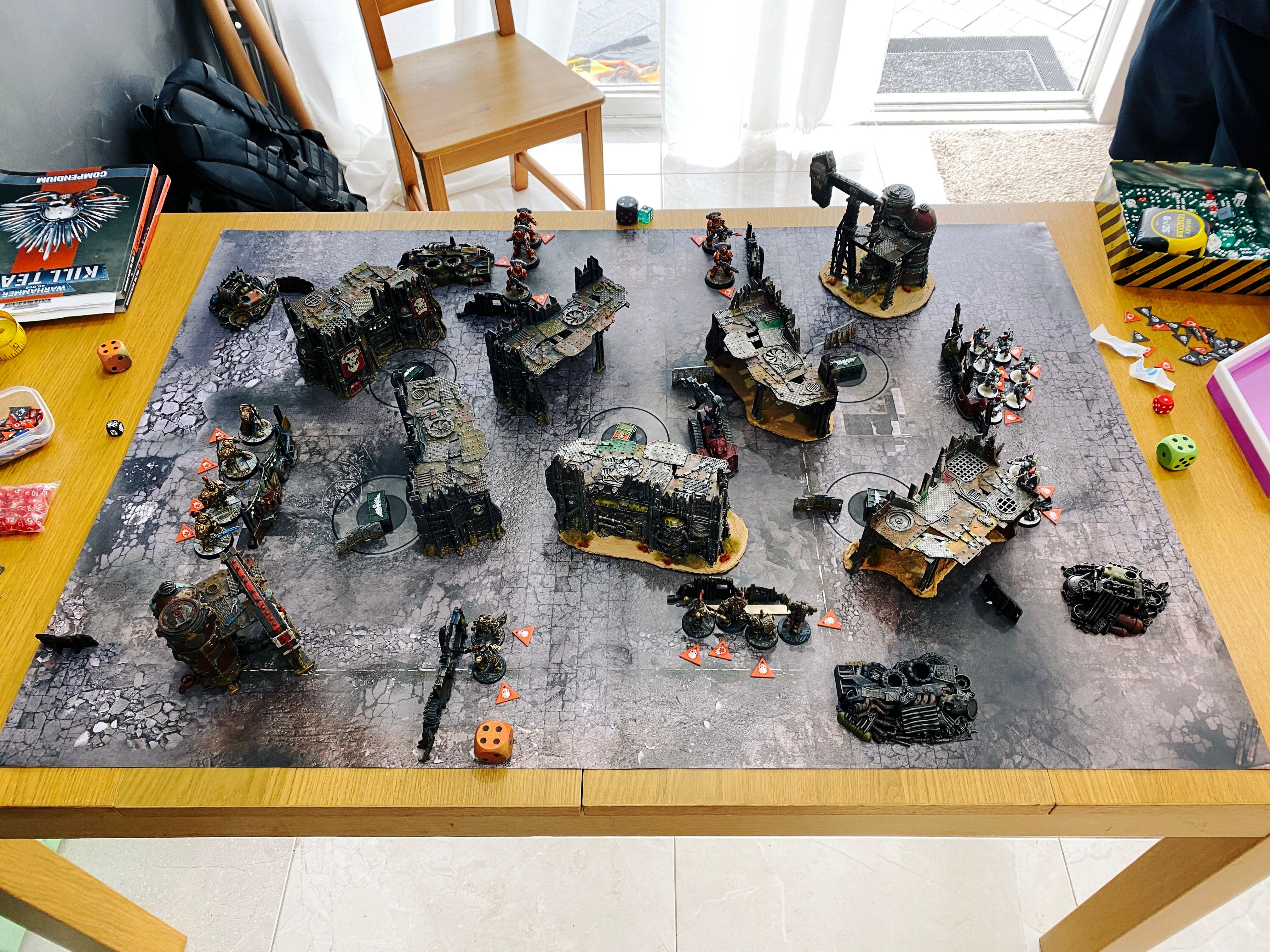 A photo of a fully set up game board of Warhammer 40,000: Kill Team. The terrain is all very ramshackle and looks like it's straight from a junkyard.