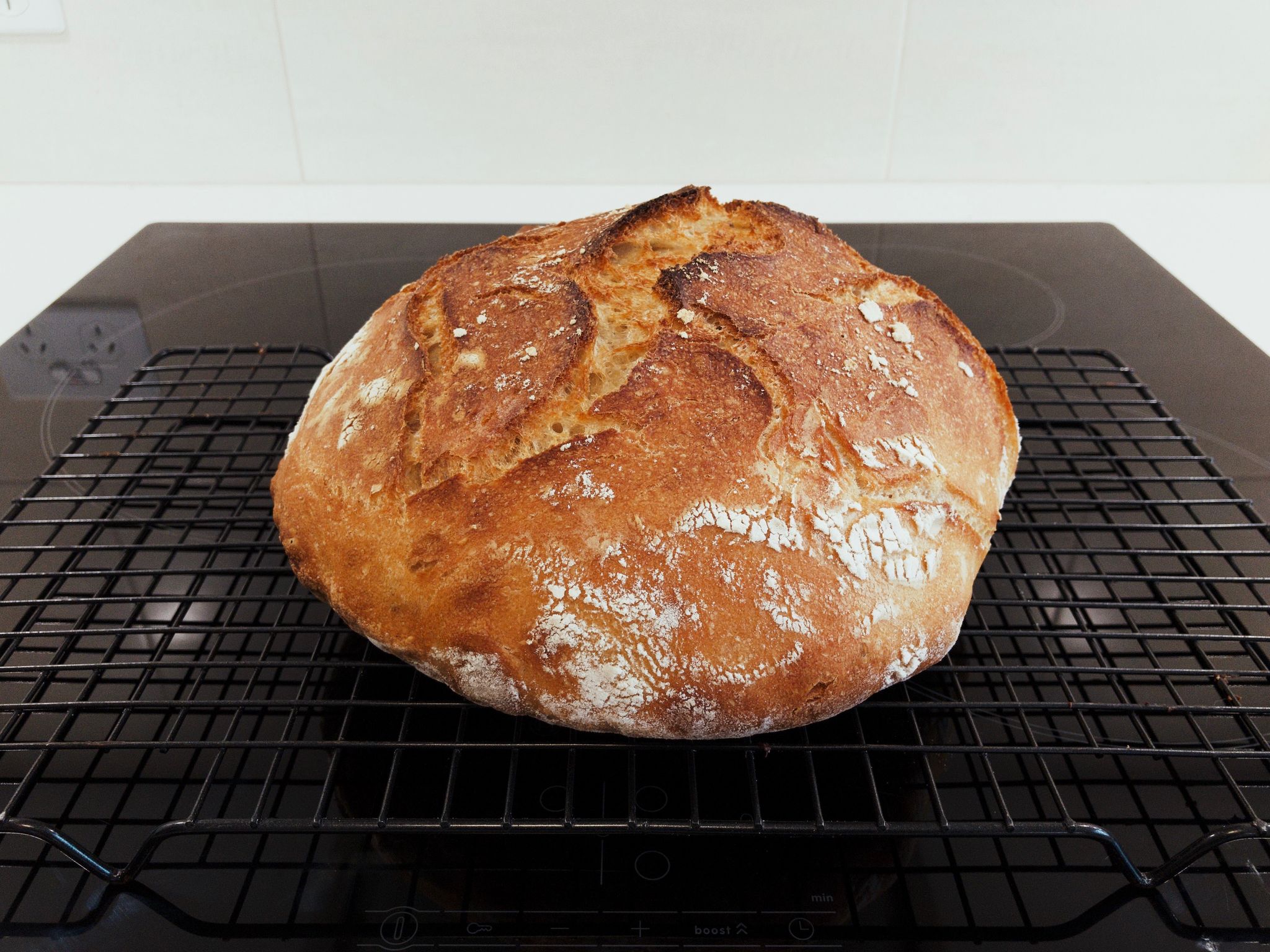A brown absolutely delicious-looking round loaf of bread sitting on a cooling rack.