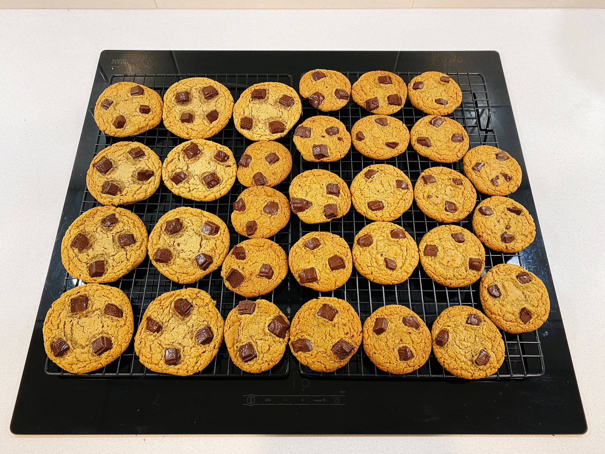 A photo of a bunch of chocolate chunk cookies sitting on a cooling rack. The ones on the left are FAR TOO BIG.