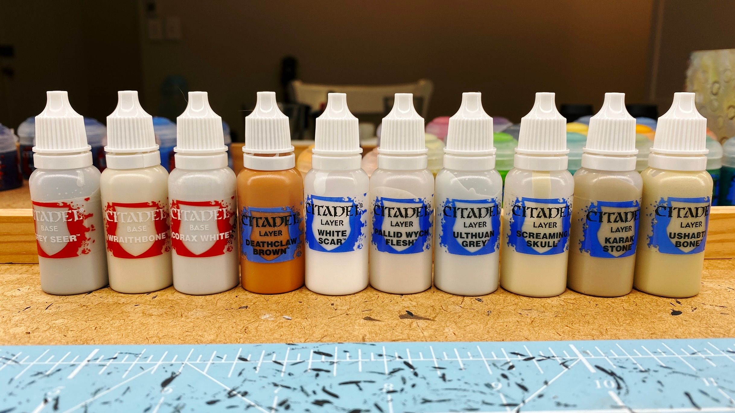 A photo of ten plastic dropper bottles with white screw tops that have various shades, mostly off-whites, of Games Workshop's "Citadel" brand paints in them. I've pulled the labels off the original pots, trimmed them, and stuck them back into the new dropper bottles.