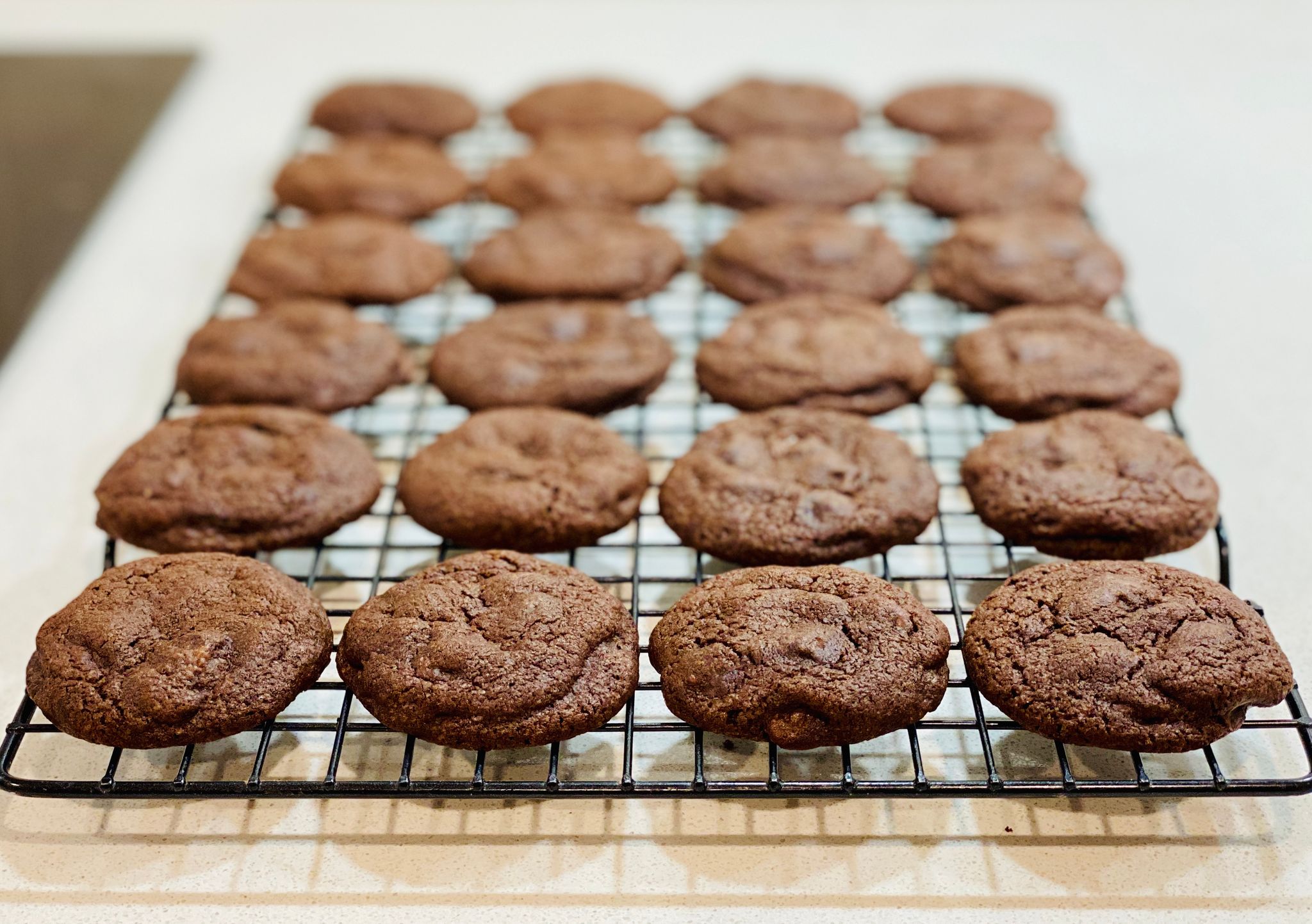 A photo of a cooling rack full of dark chocolate cookies.