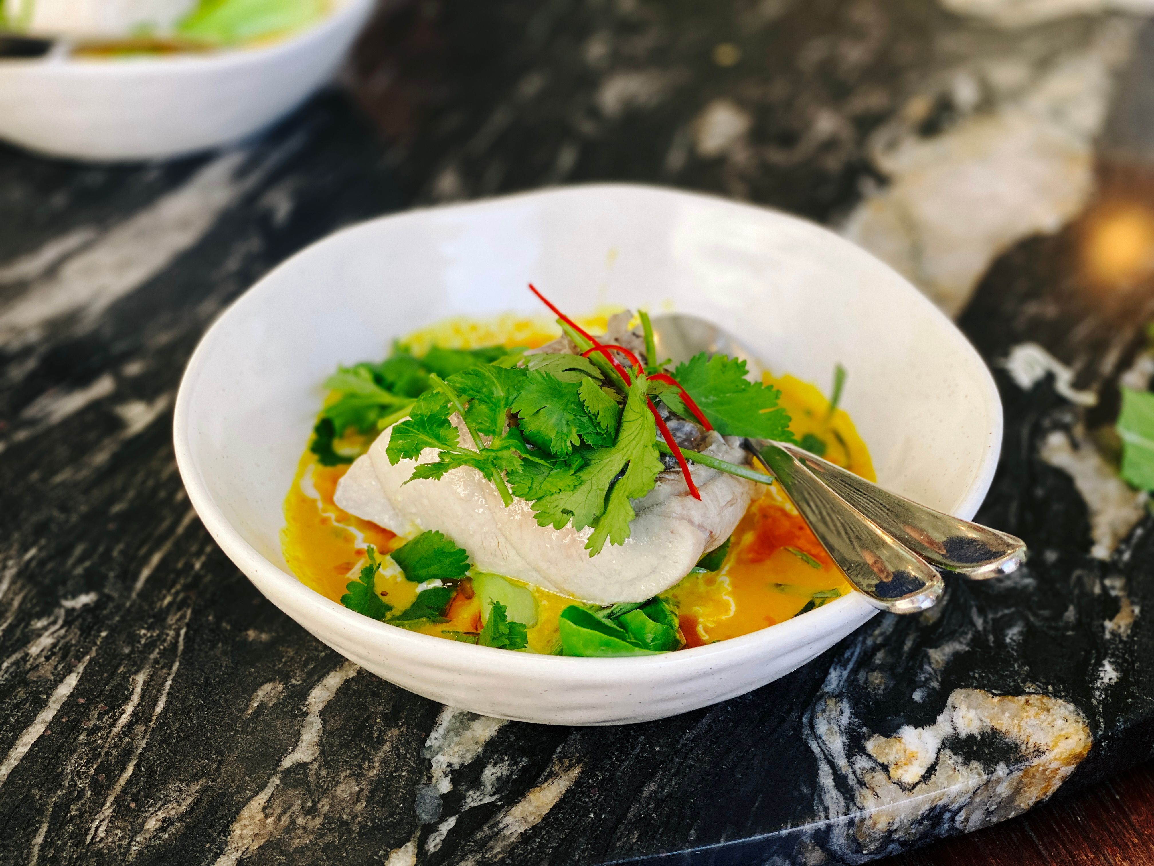 A photo of a bowl with a big chunk of steamed white fish, with turmeric and lemongrass curry, and baby bok choy.
