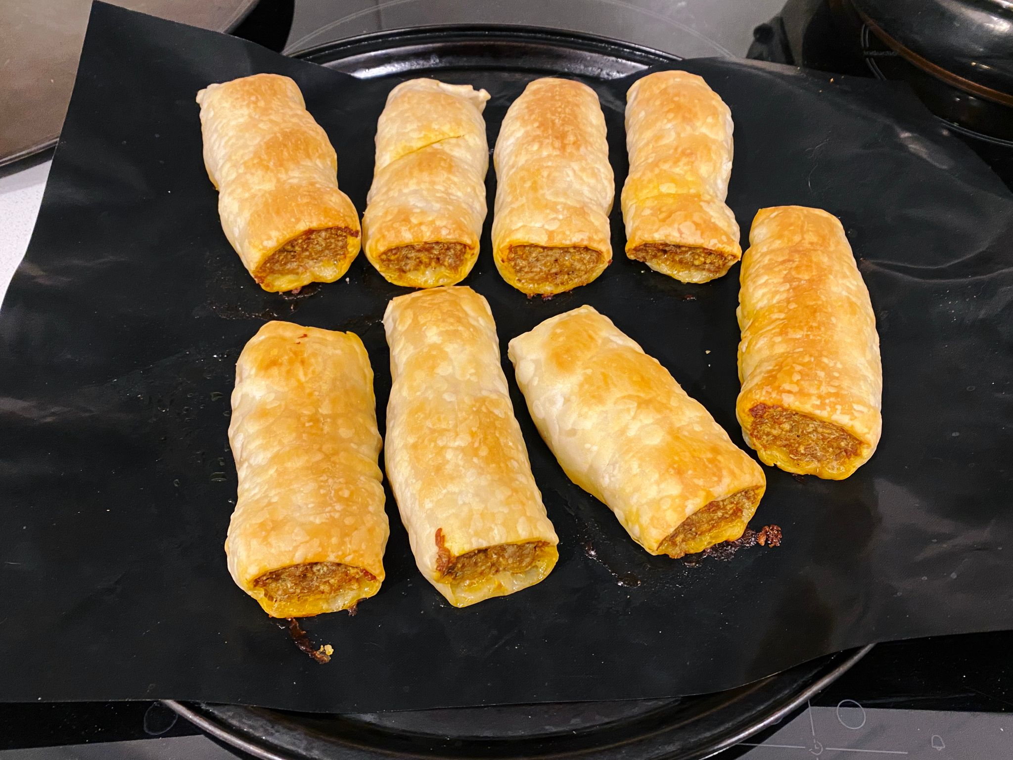 A photo of eight sausage rolls sitting an oven tray, fresh out of the oven.