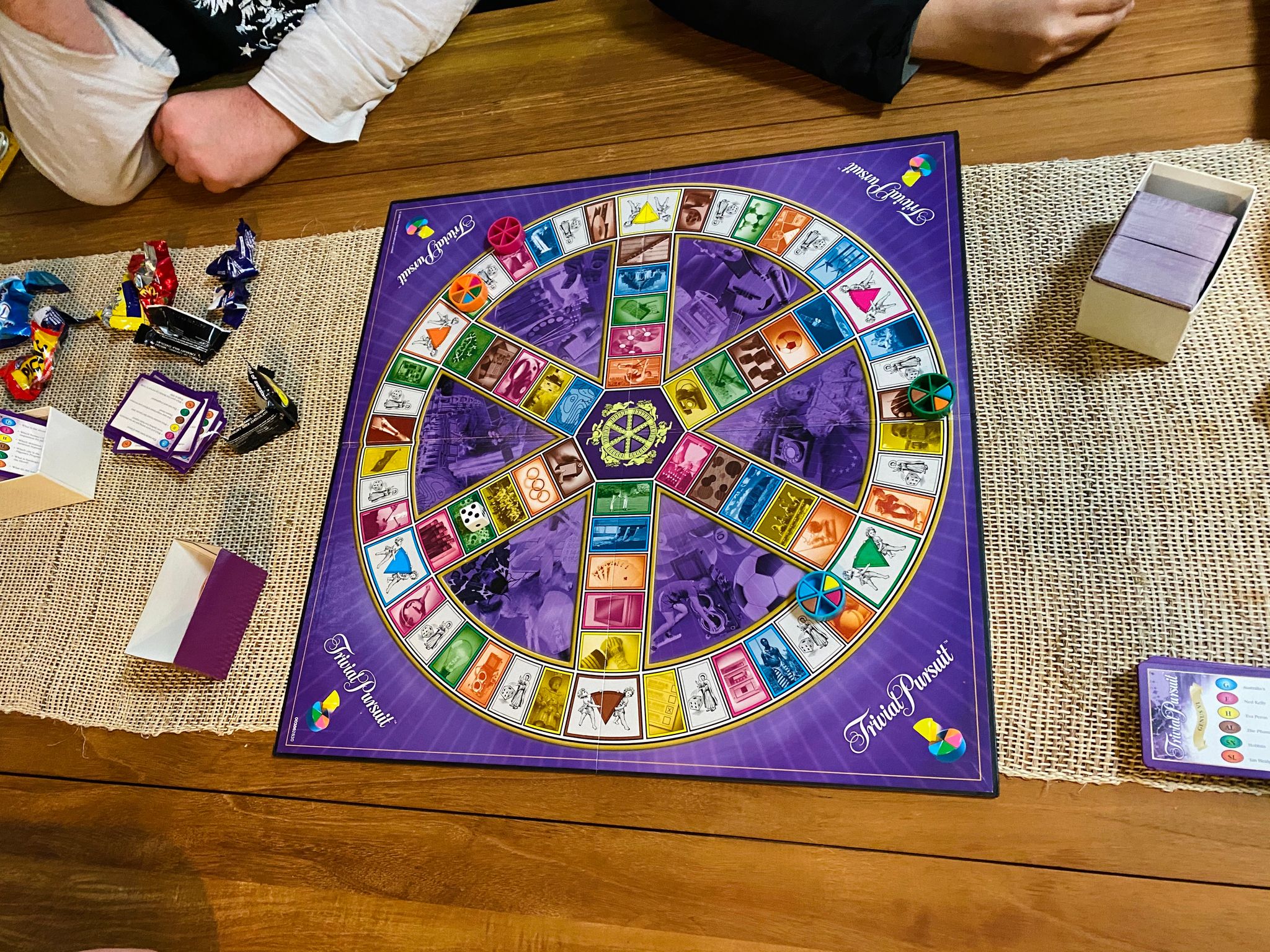 A photo of a Trivial Pursuit board and pieces on a table.