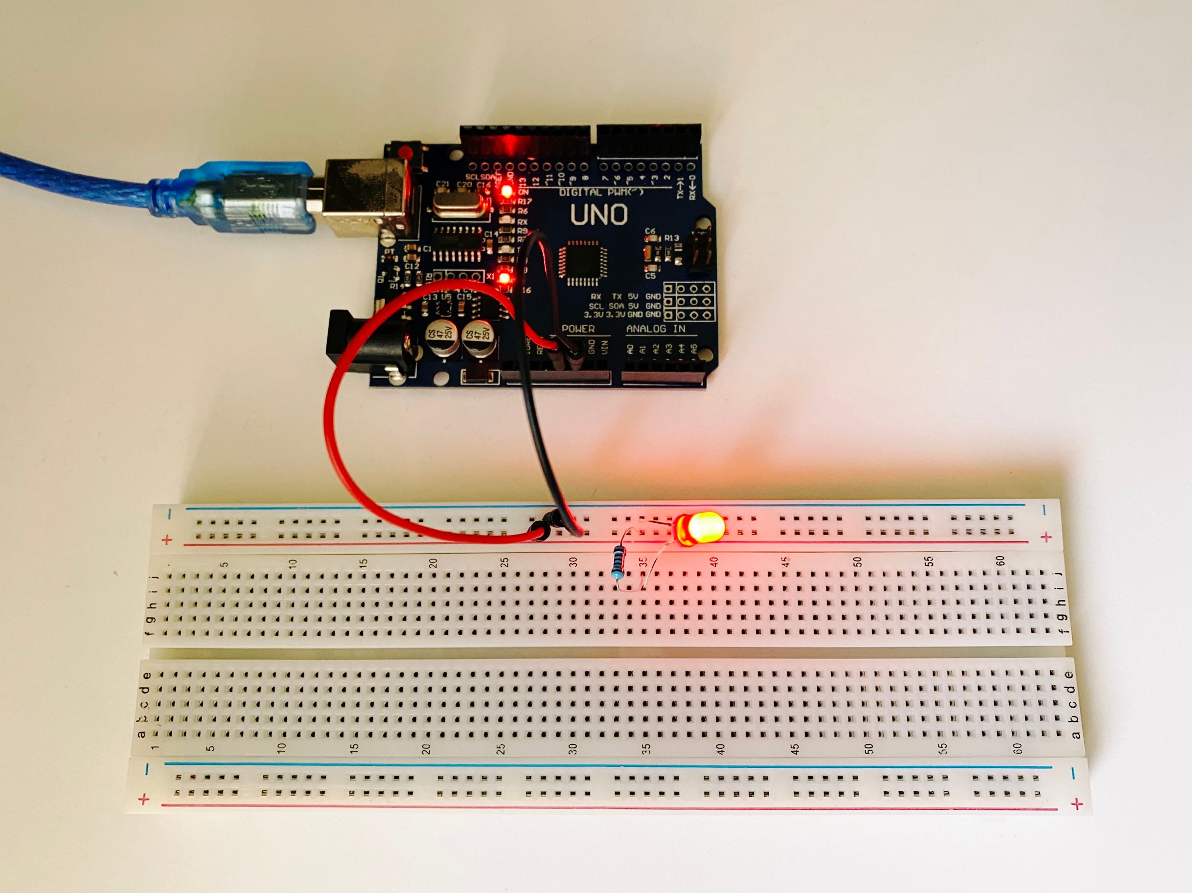 A photo of an Arduino connected to a breadboard that has a resistor and a red LED plugged into it. The LED is lit up.