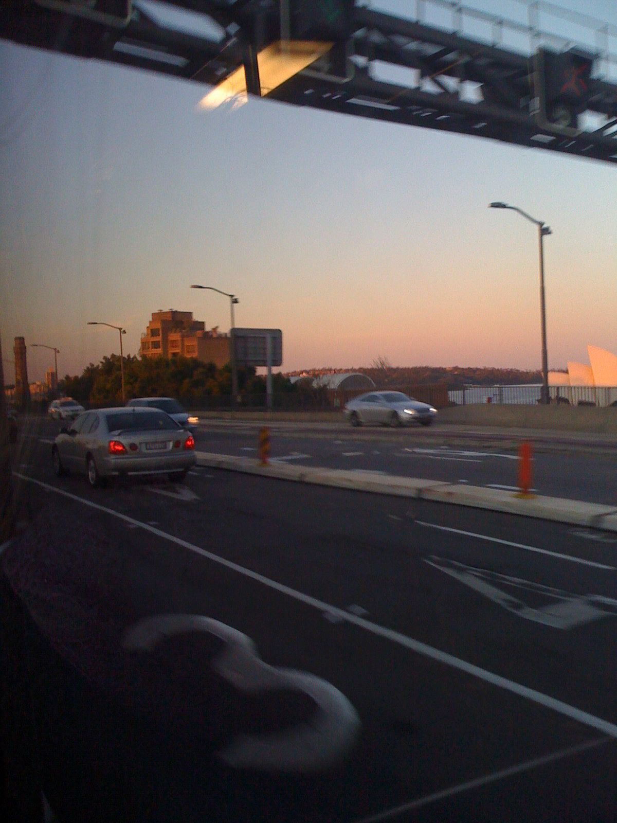 A photo looking out the window of a bus having just gotten off the Sydney Harbour Bridge. It's sunset.