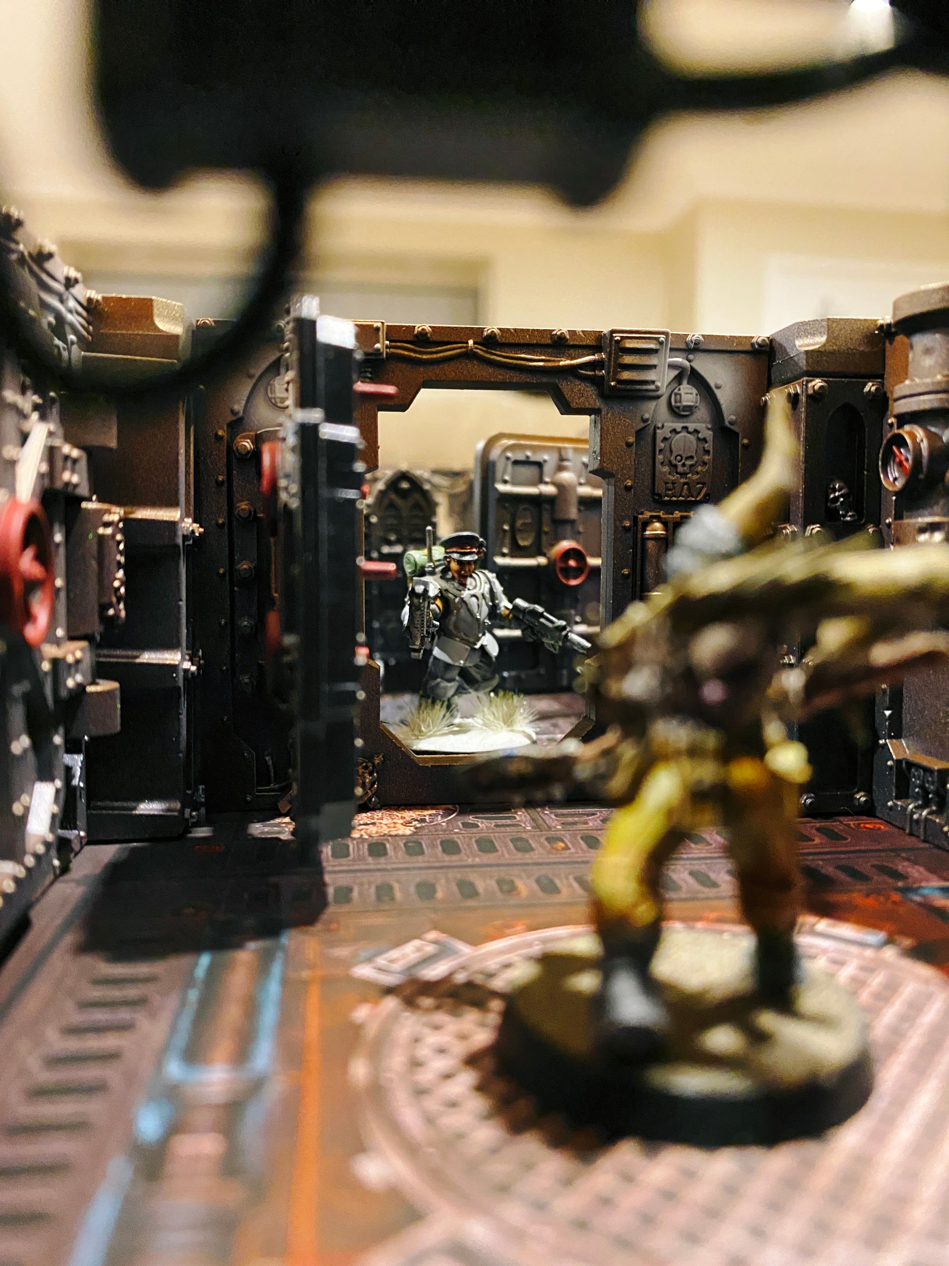 Another even closer-upper shot, taken from the point of view of one of the miniatures. A different female warrior in armour is pointing her gun through a hatchway at a Poxwalker, which is a gross pustle-covered zombie thing.