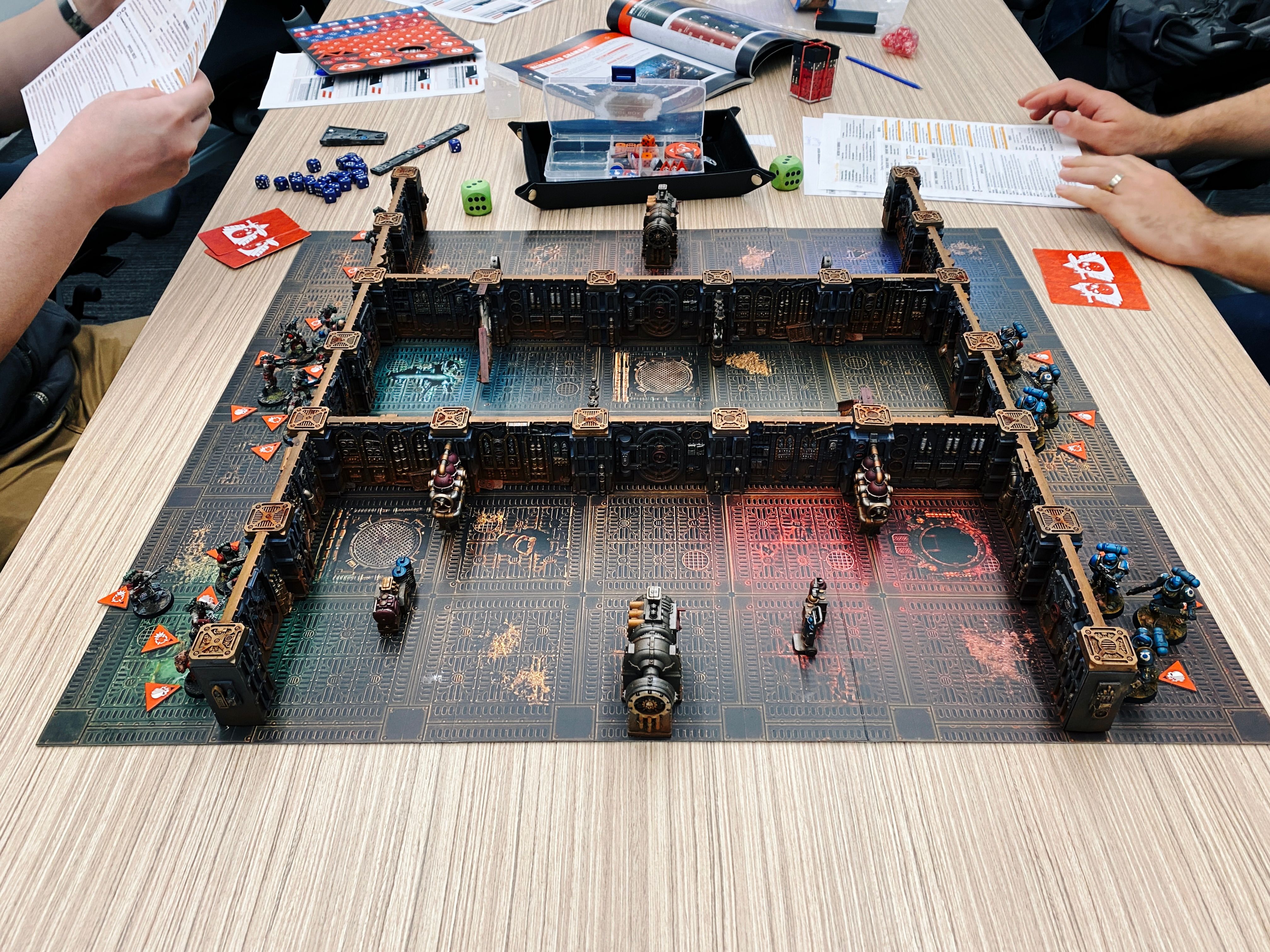 A photo of the board of Warhammer 40,000: Kill Team's new box called "Into the Dark". There's a bunch of walls that are incredibly detailed and look almost steampunk, with hulking Space Marines on the right and regular armoured human troops on the left.