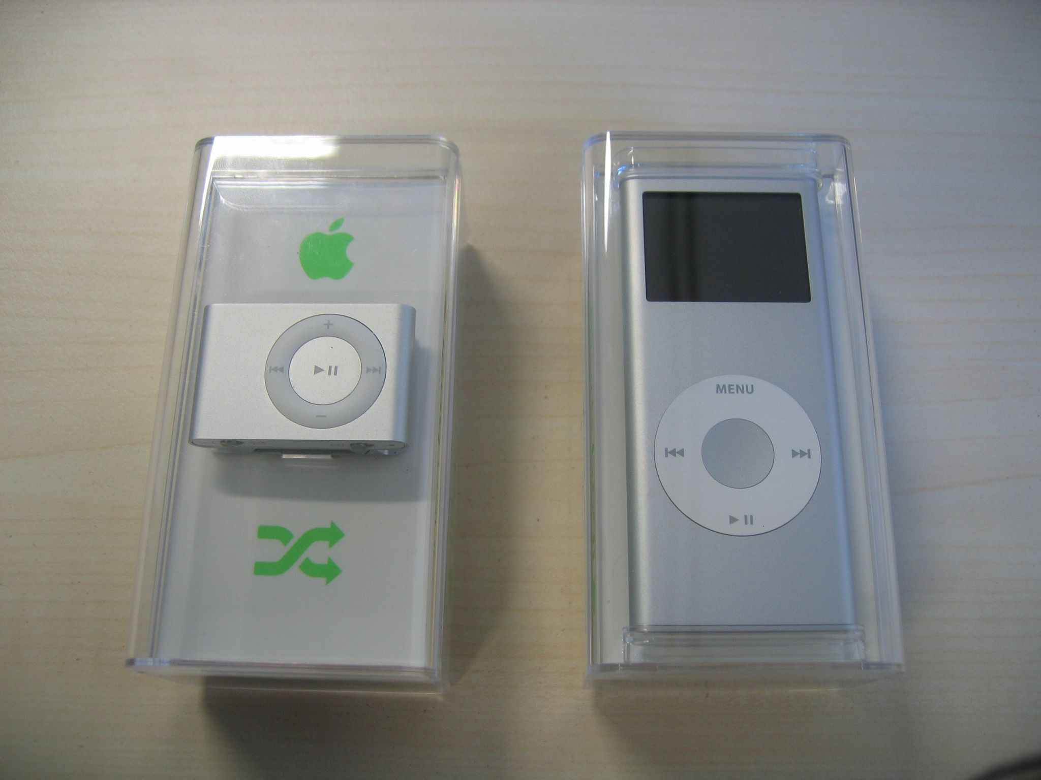 A photo of a silver second-generation iPod shuffle, and a silver second-generation iPod nano, both in their original packaging.