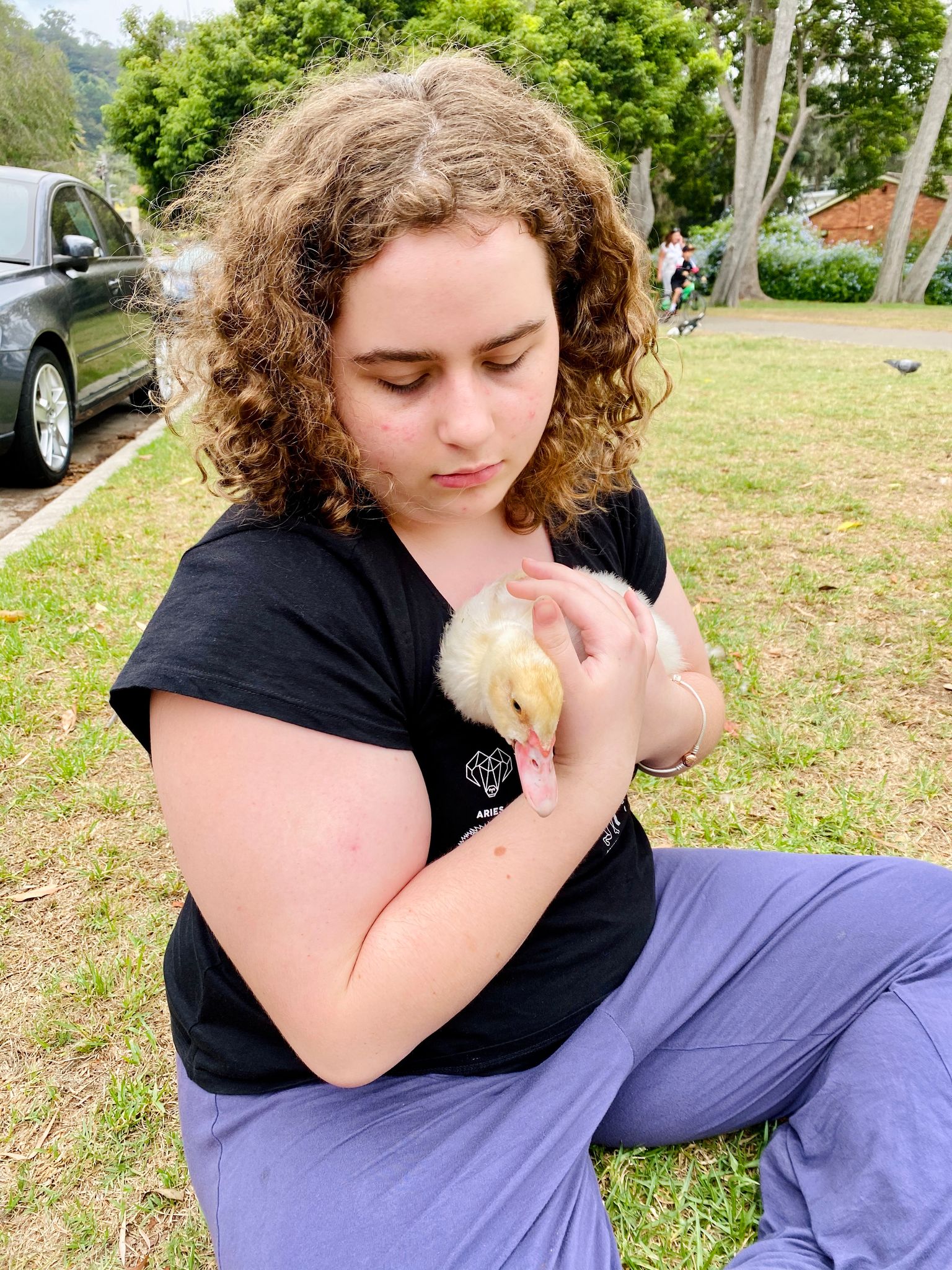 A photo of a light brown-haired white girl holding a fluffy not-quite-duckling.