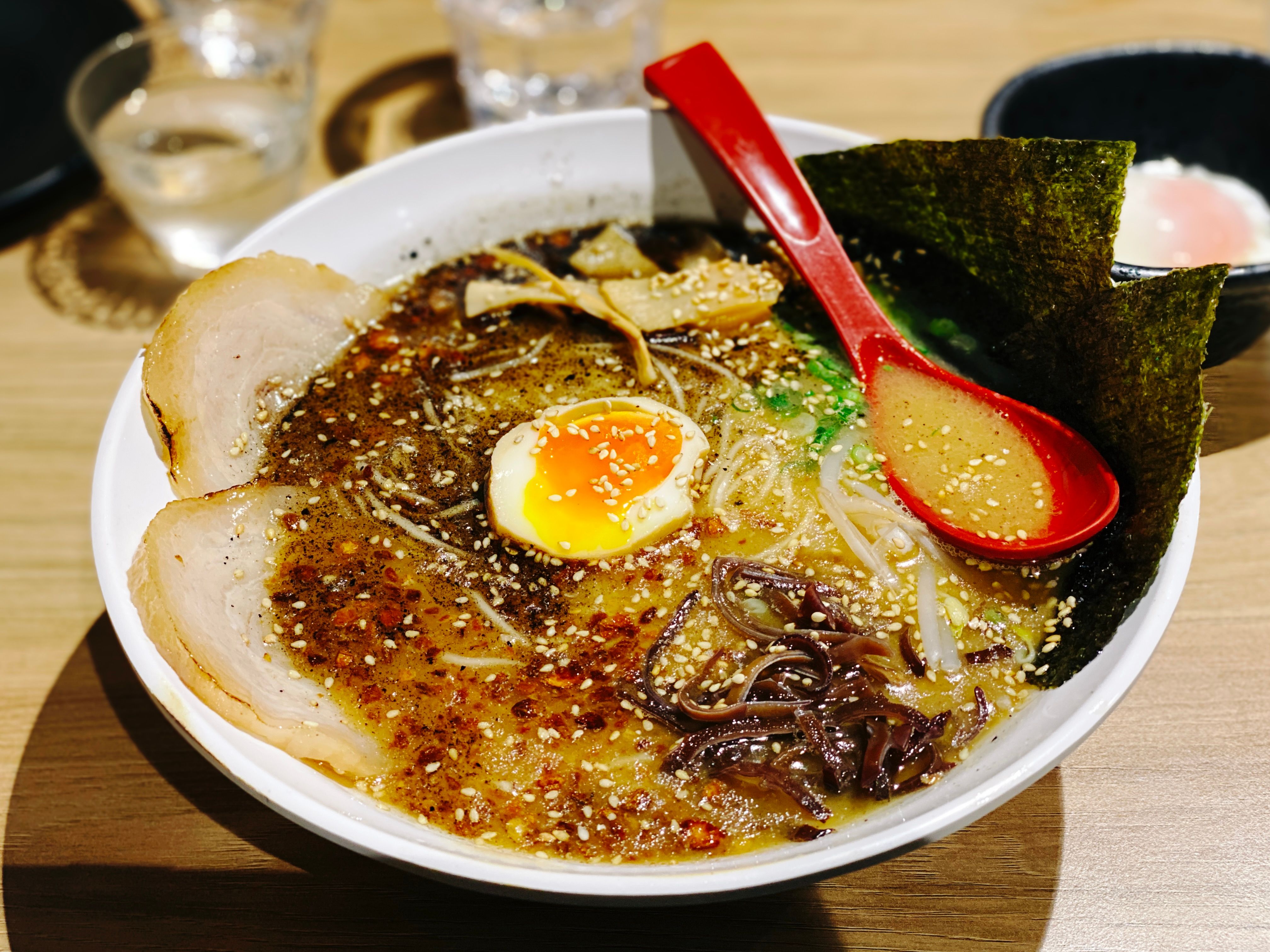 A photo of a big bowl of black garlic ramen with a soft-boiled egg on top.