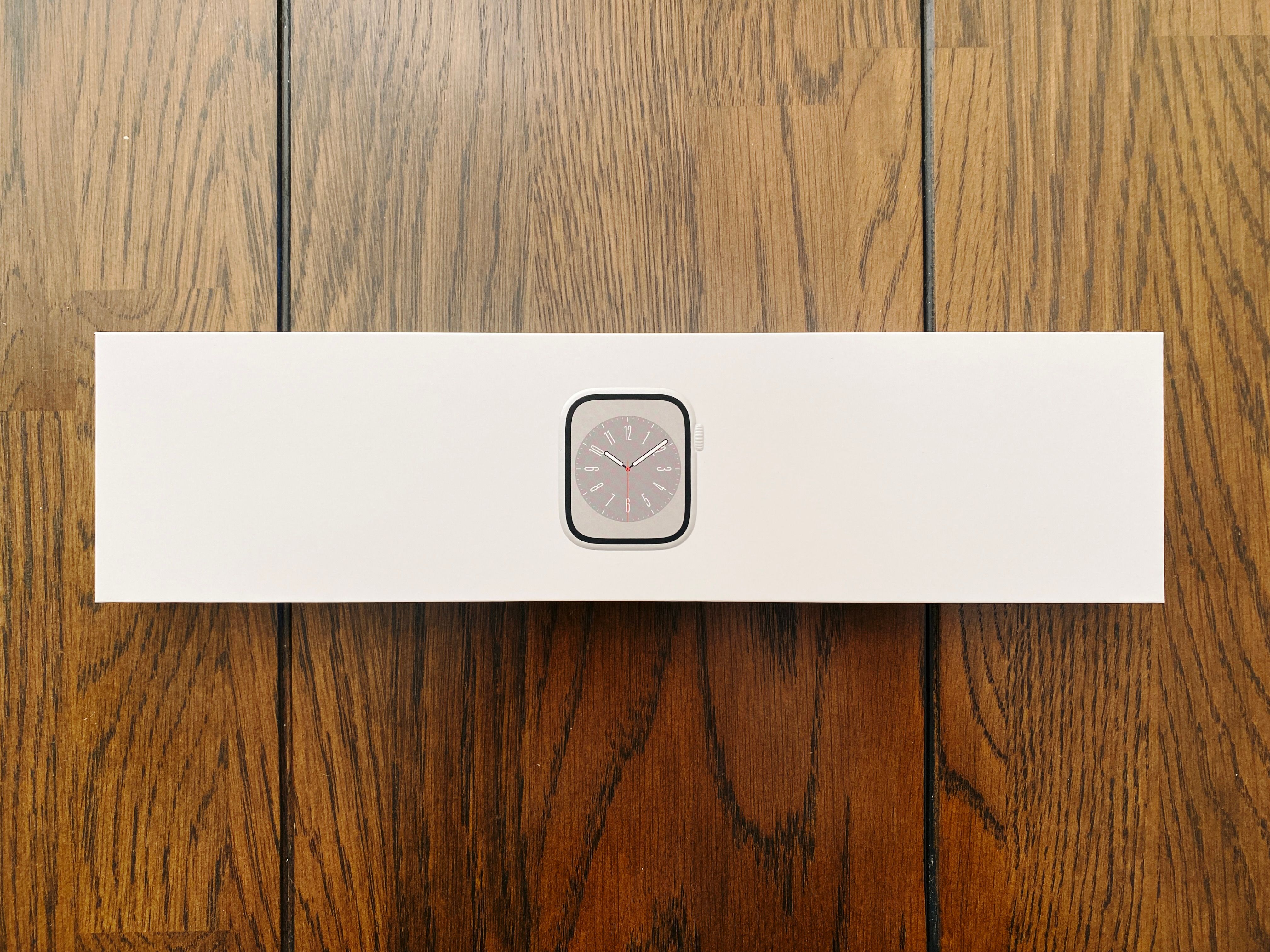 A photo of a long and narrow white cardboard box with an image of a stainless steel Apple Watch on the front of it.