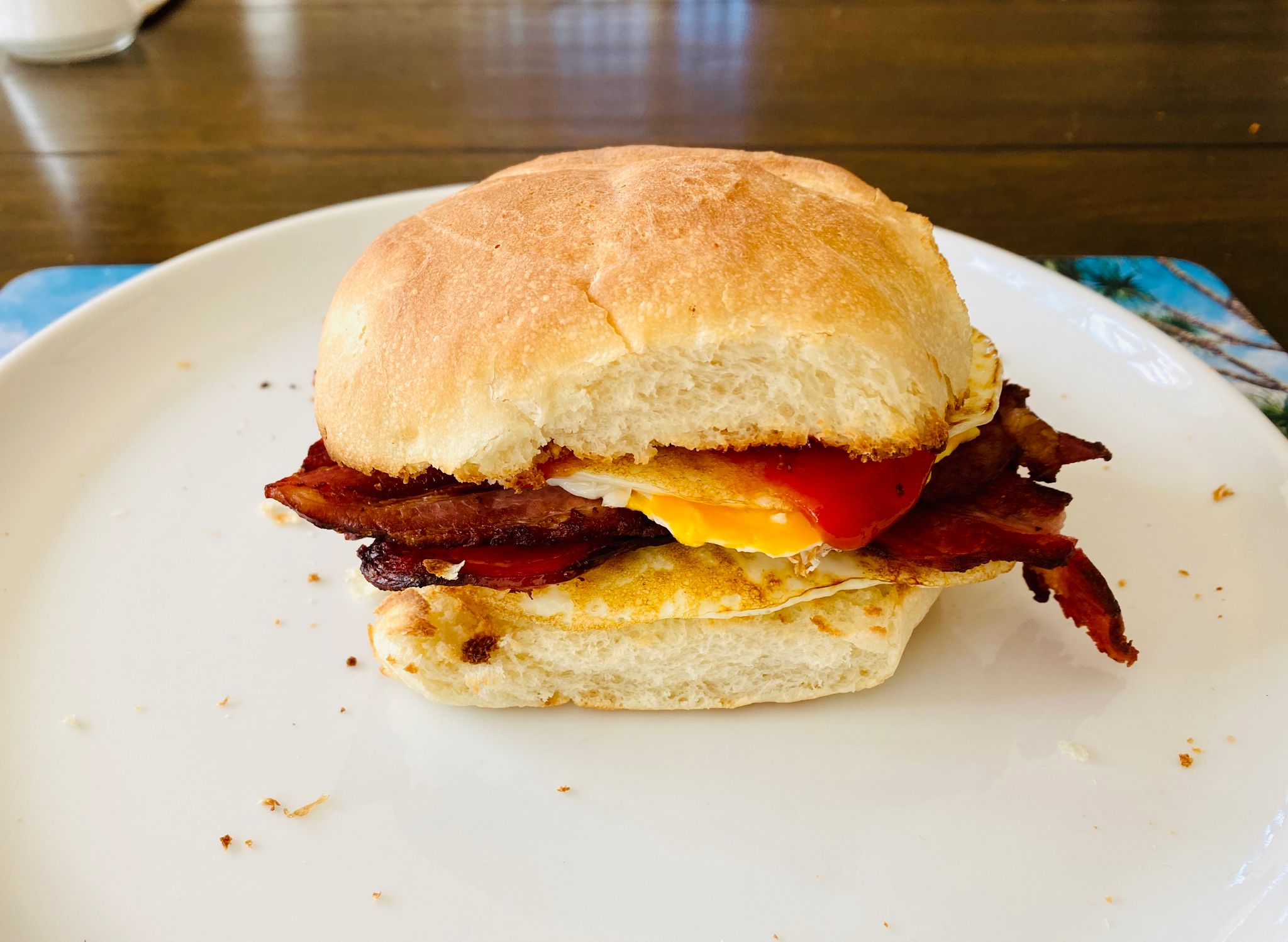 A photo of a bacon and egg roll sitting on a plate, with a little bit of ketchup just visible.