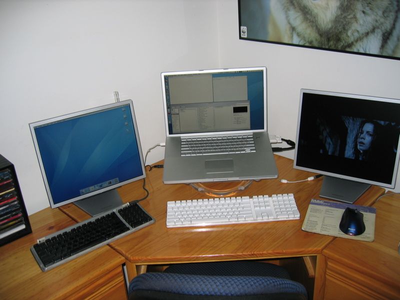 A closeup of the main computer setup showing just the laptop and two monitors, plus a white Apple keyboard in front of the laptop.