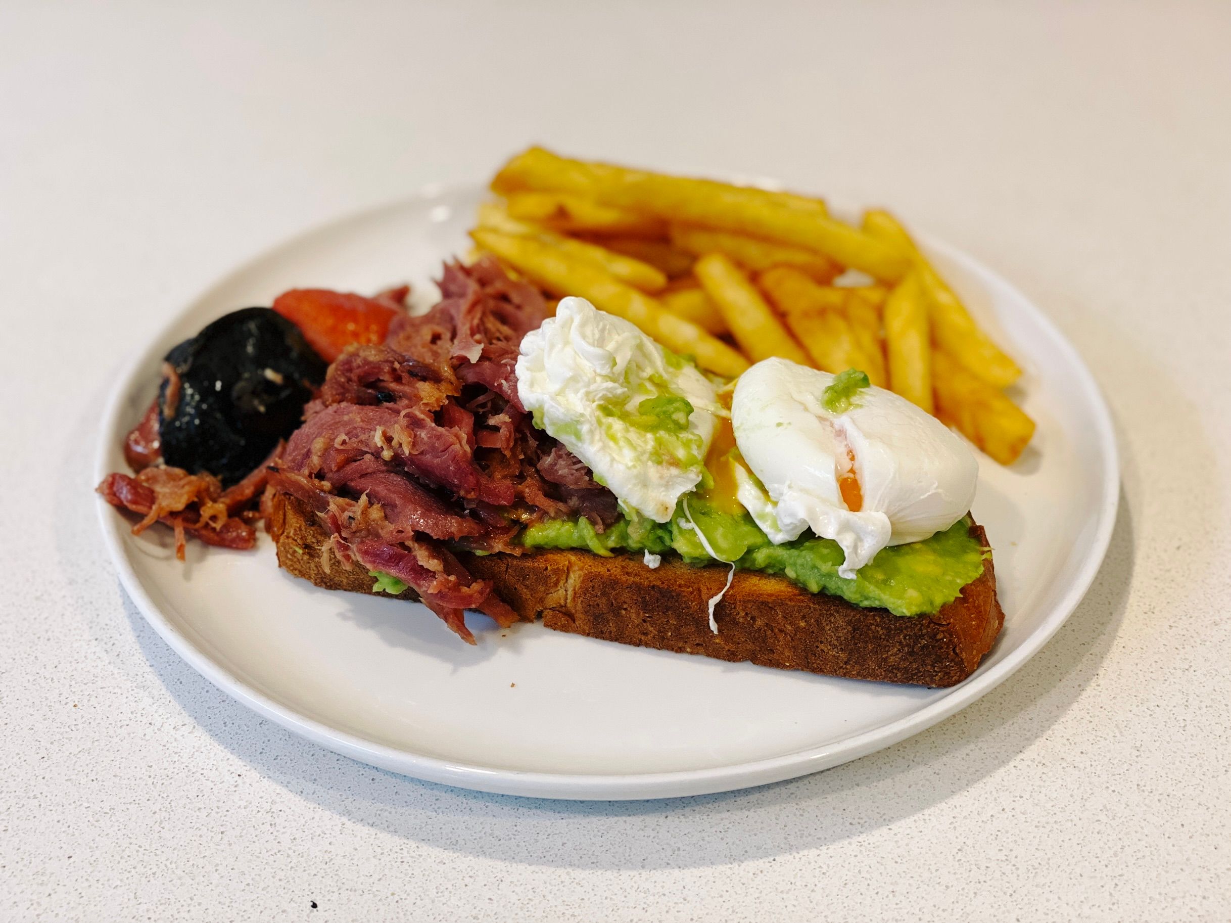 A photo of a thick slice of rye bread covered in smashed avocado with two poached eggs on one side and something that looks like corned beef (but isn't, I'm not entirely sure what it was but it was delicious) on the other, and hot chips sitting behind it.