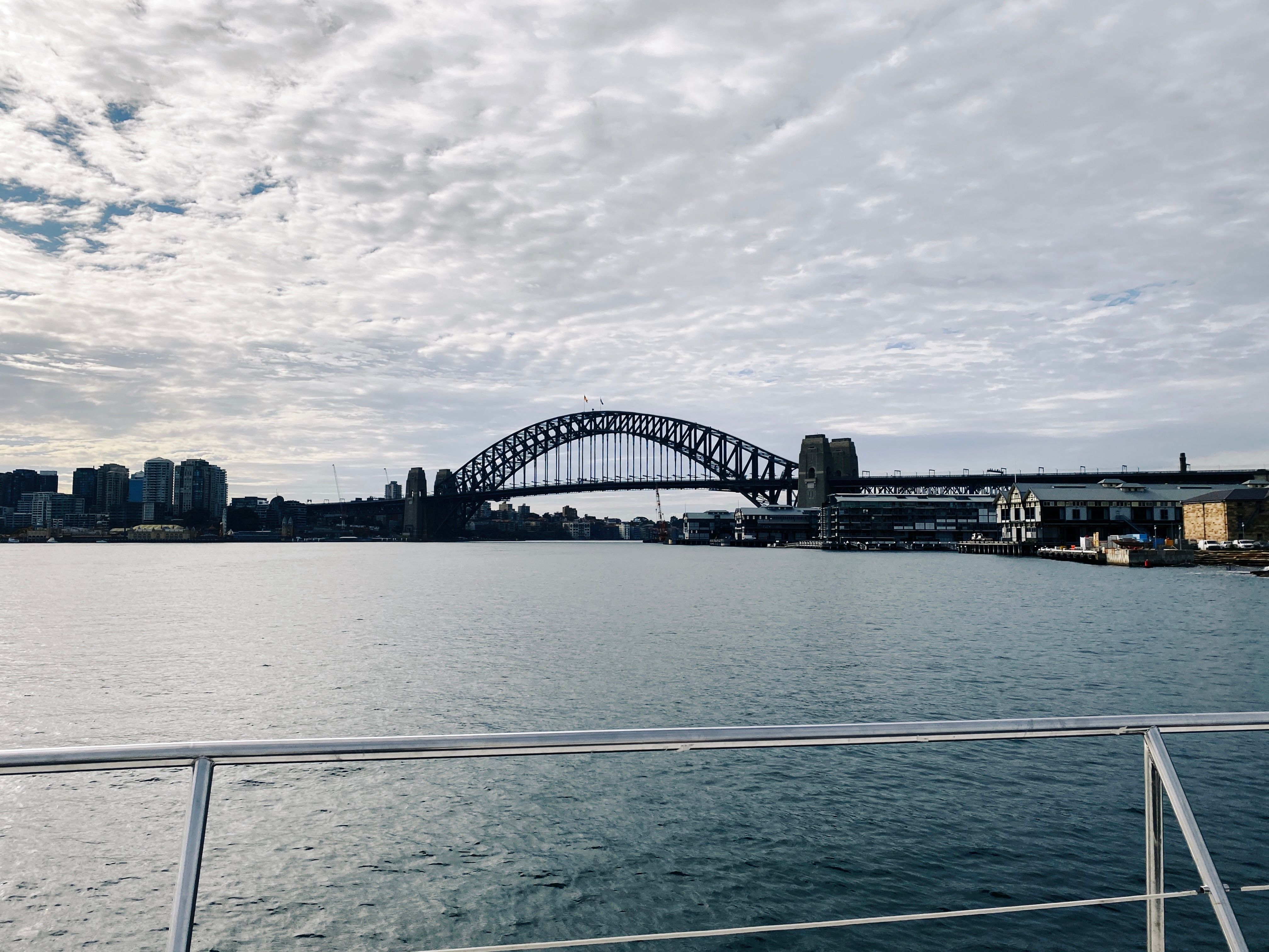 A photo of the Sydney Harbour Bridge taken from a boat. The sky is grey and mostly overcast.