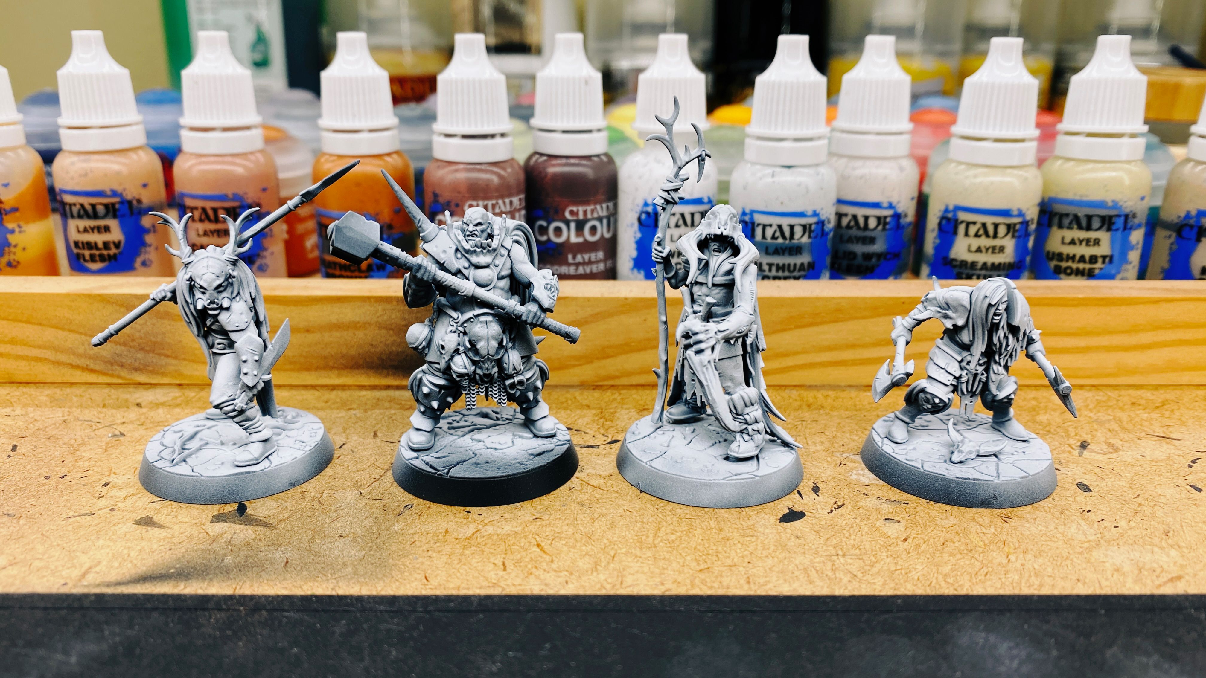 A photo of the four shamanistic-looking warriors of the Warhammer Underworlds warband the Gnarlspirit Pack. They're all dressed in leathers and furs and the leader has a large animal skull on his head. His left arm is too slightly larger than normal and looks like something out of the movie Aliens, and is wielding/has growing out of the hand a blade that looks like it may be bone.
