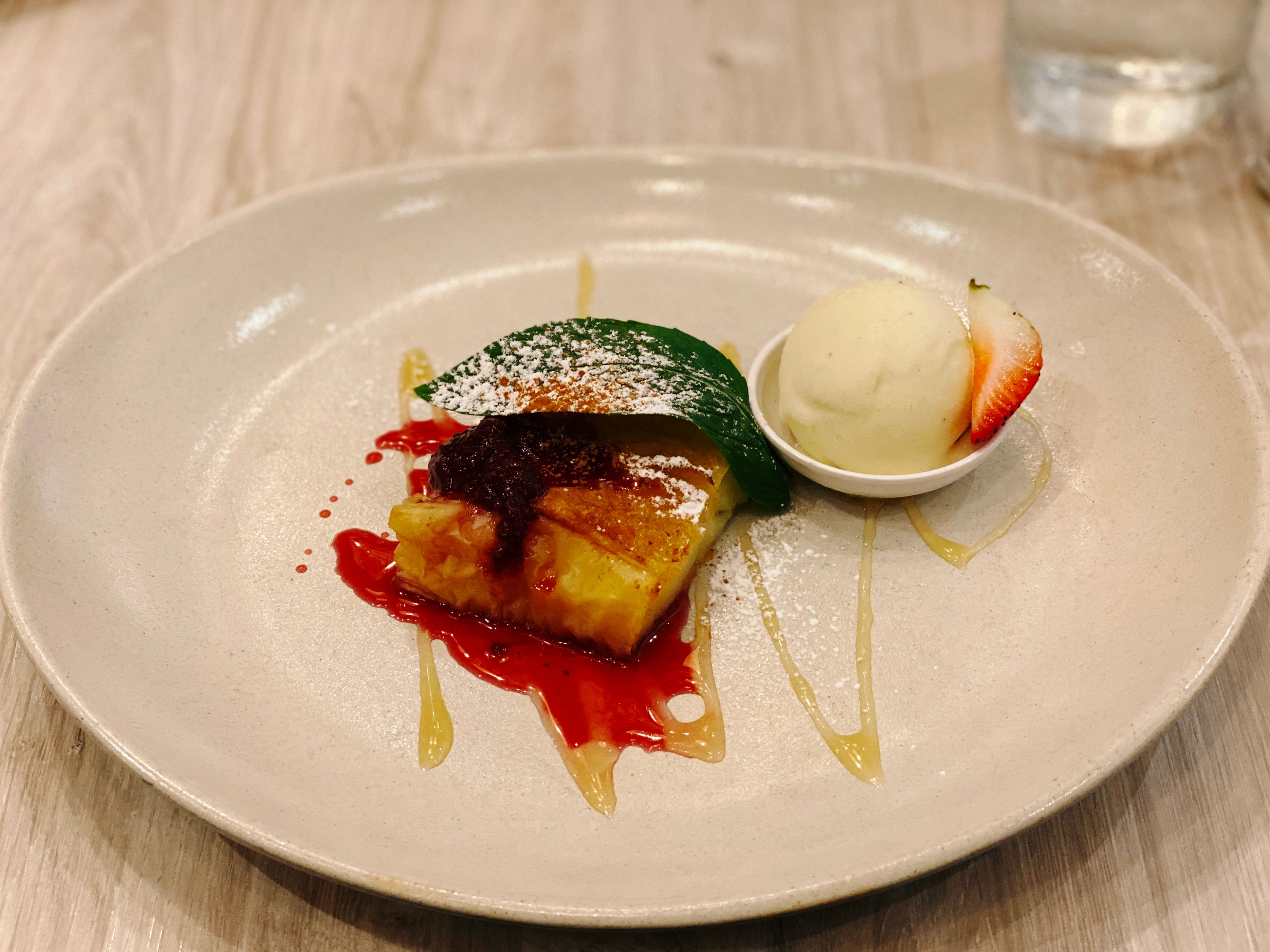 A photo of galaktoboureko, which is a Greek dessert made of filo pastry and filled with semolina custard. There's a berry compote on it and some vanilla bean ice cream next to it.