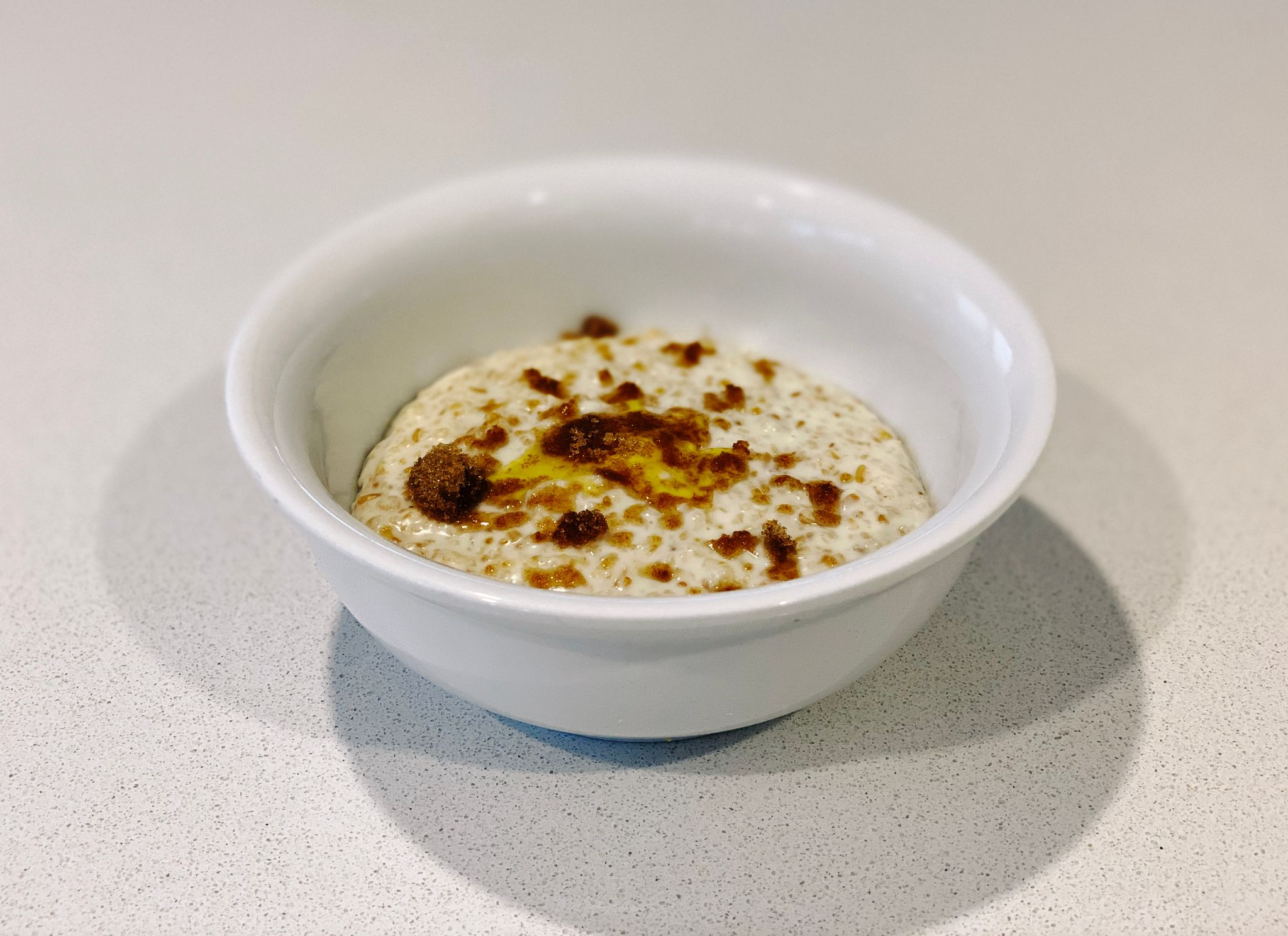 A photo of a bowl of porridge, topped with brown sugar and a bit of butter that's now melted.